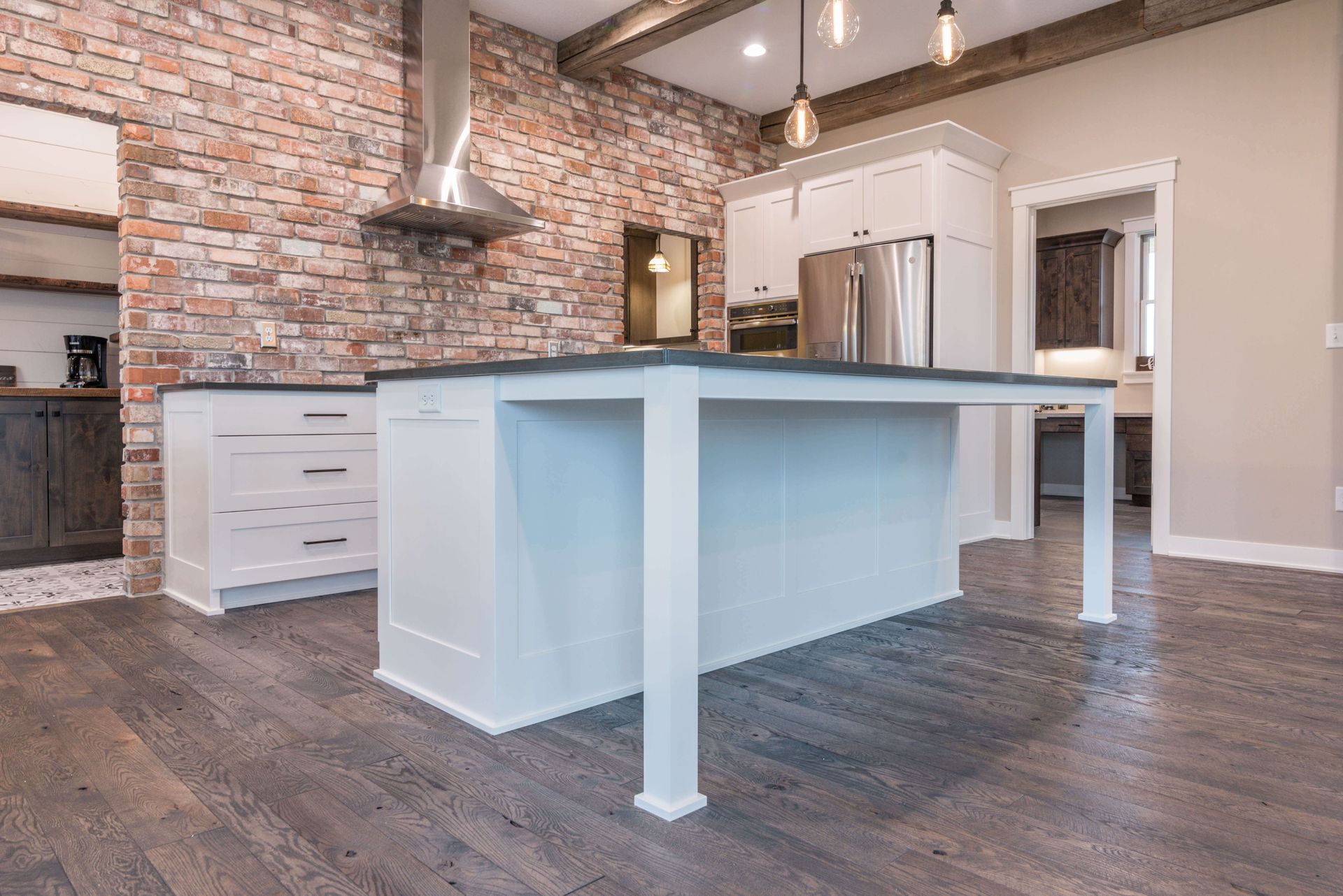 Modern kitchen with brick wall, white cabinets, and island with dark countertop.
