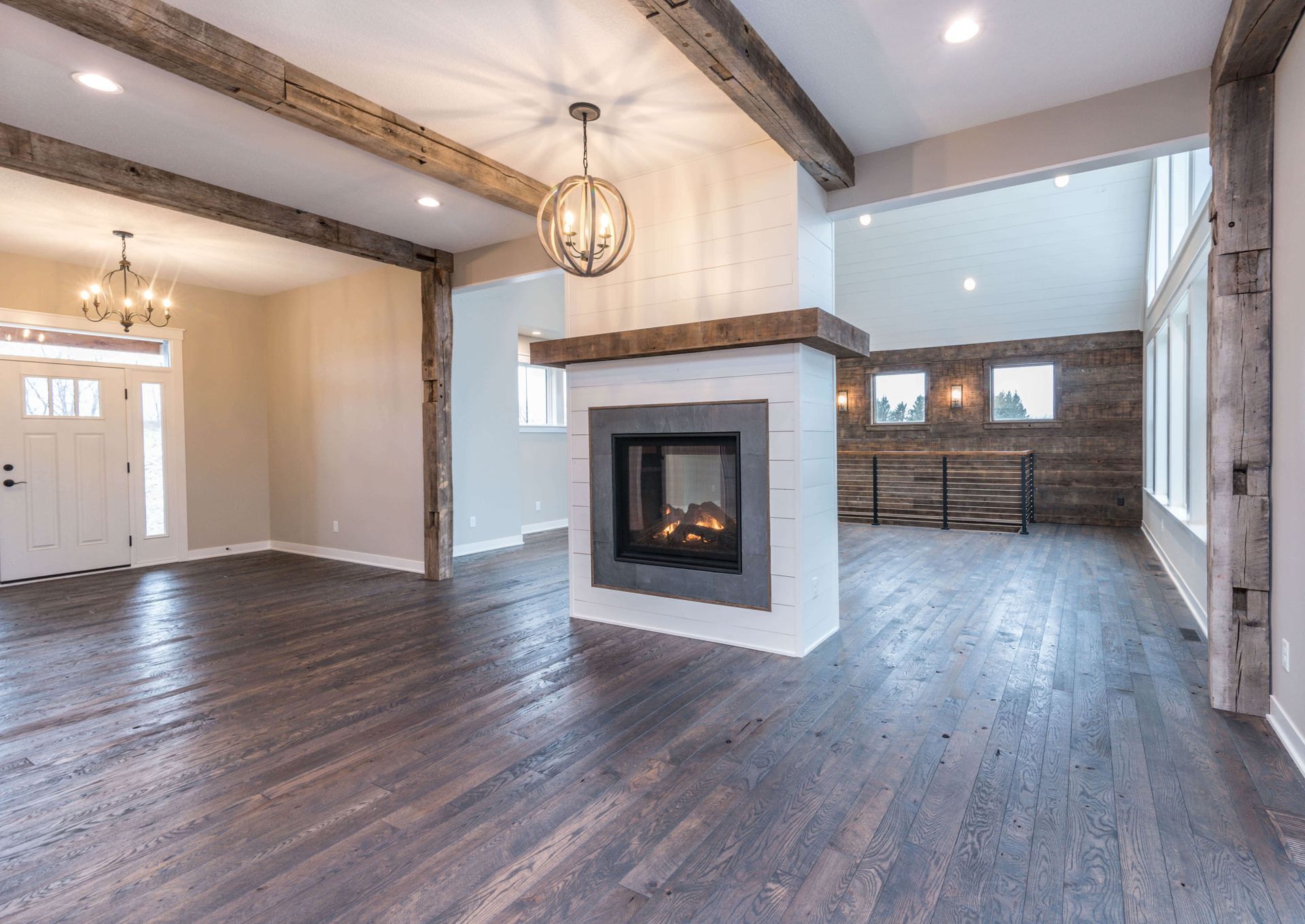 Spacious living room with a fireplace, wooden beams, hardwood floors, and large windows.