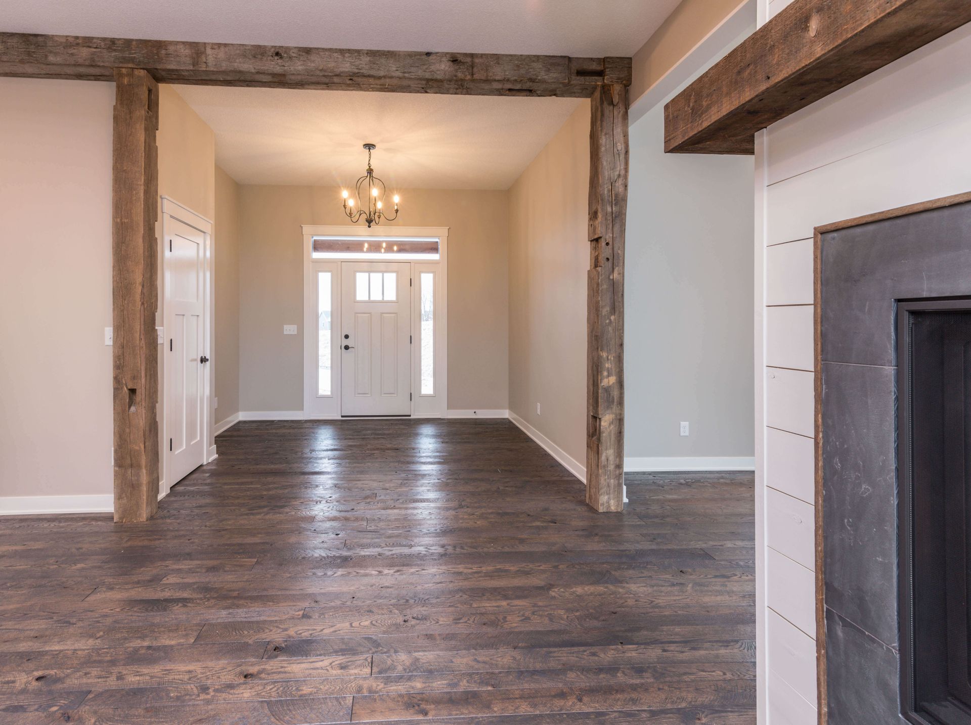Interior with rustic wood beams, light-colored walls, wood floor, and chandelier in entryway.