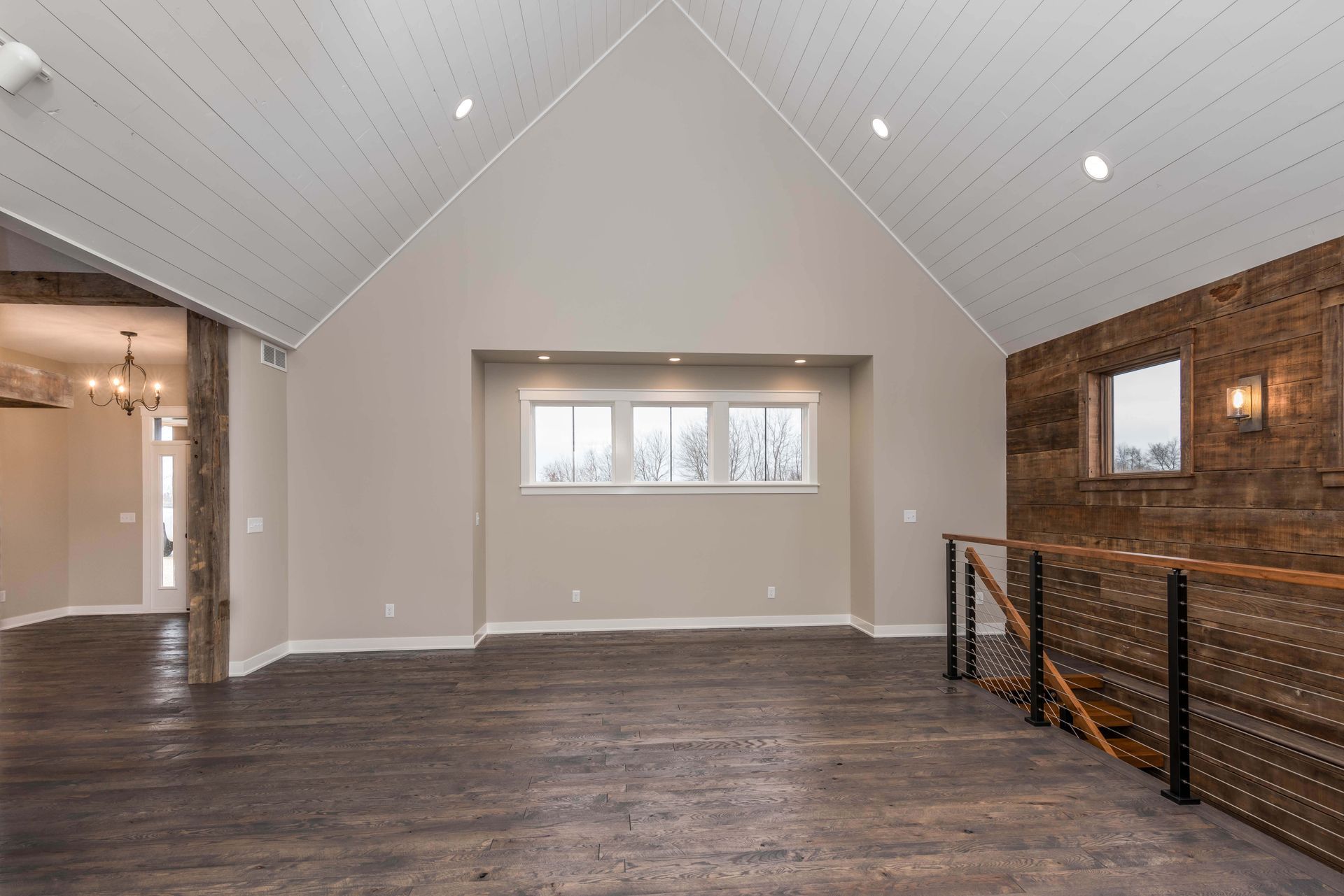 Spacious room with high, angled ceiling, a wood accent wall, and three windows; hardwood floor.