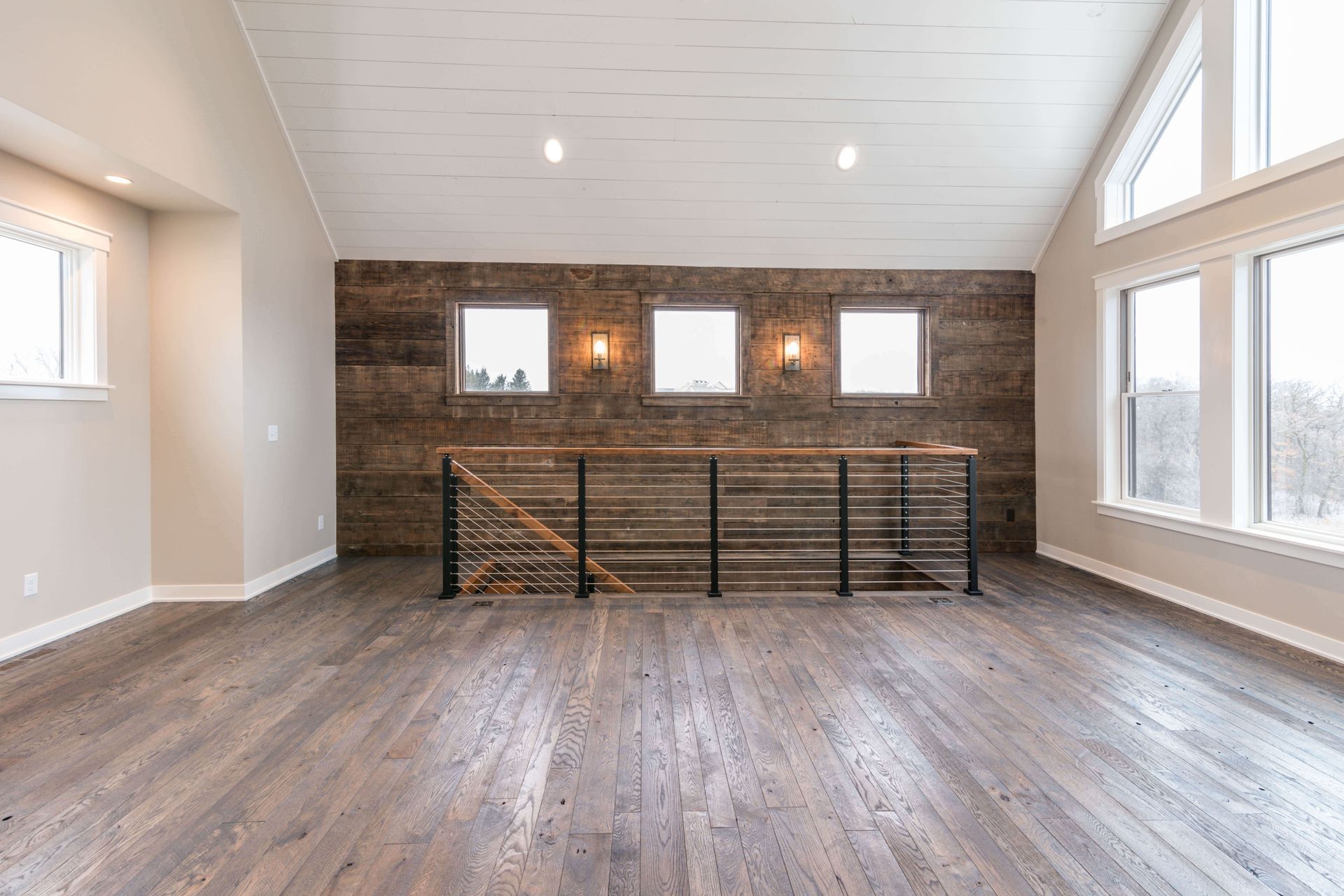 Interior with wood-paneled wall, three windows, hardwood floor, and a railing.