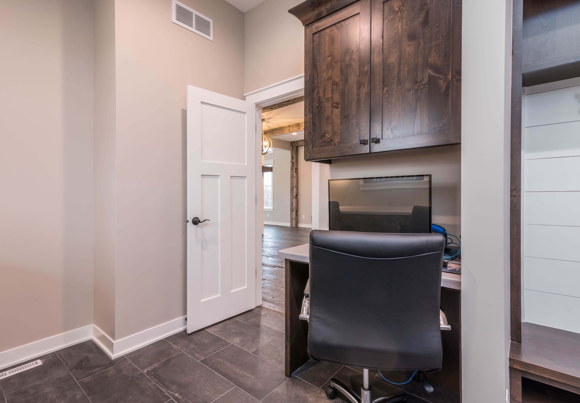 Home office with desk, dark wood cabinets, door to another room, gray walls, and dark tile floor.