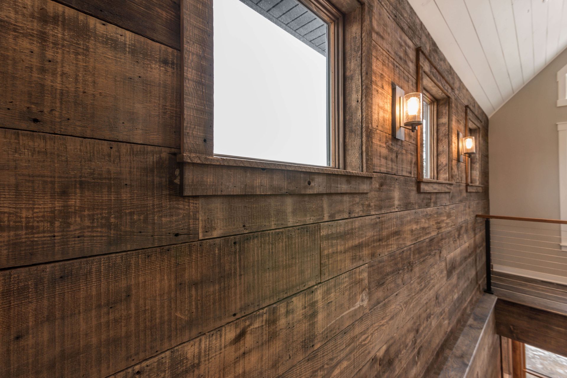 Wooden wall with two windows and sconce lights in a hallway.