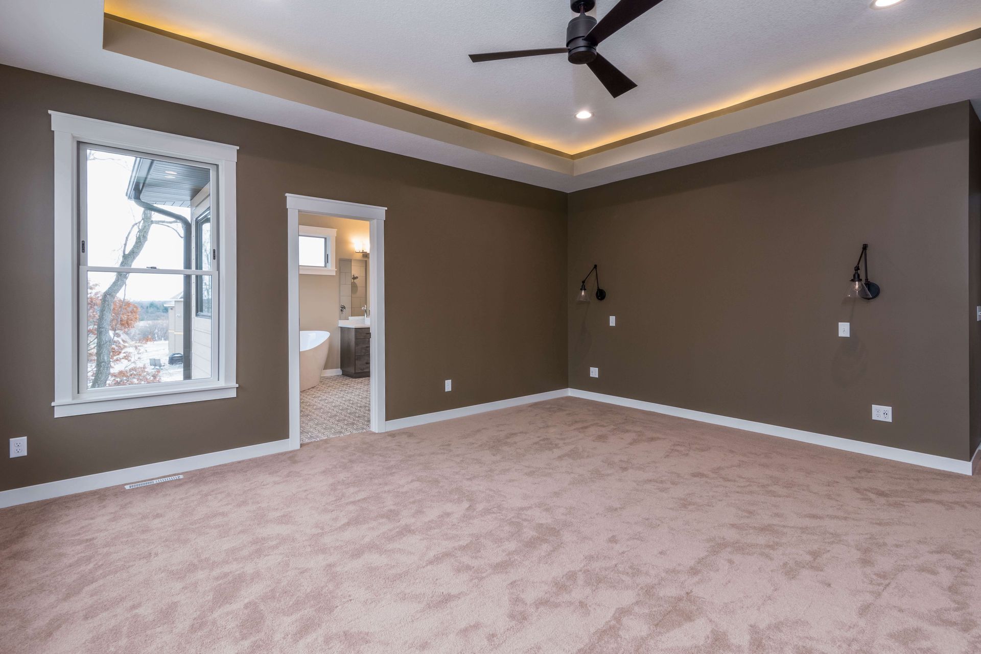 Empty bedroom with brown walls, tan carpet, and a window overlooking a winter landscape.