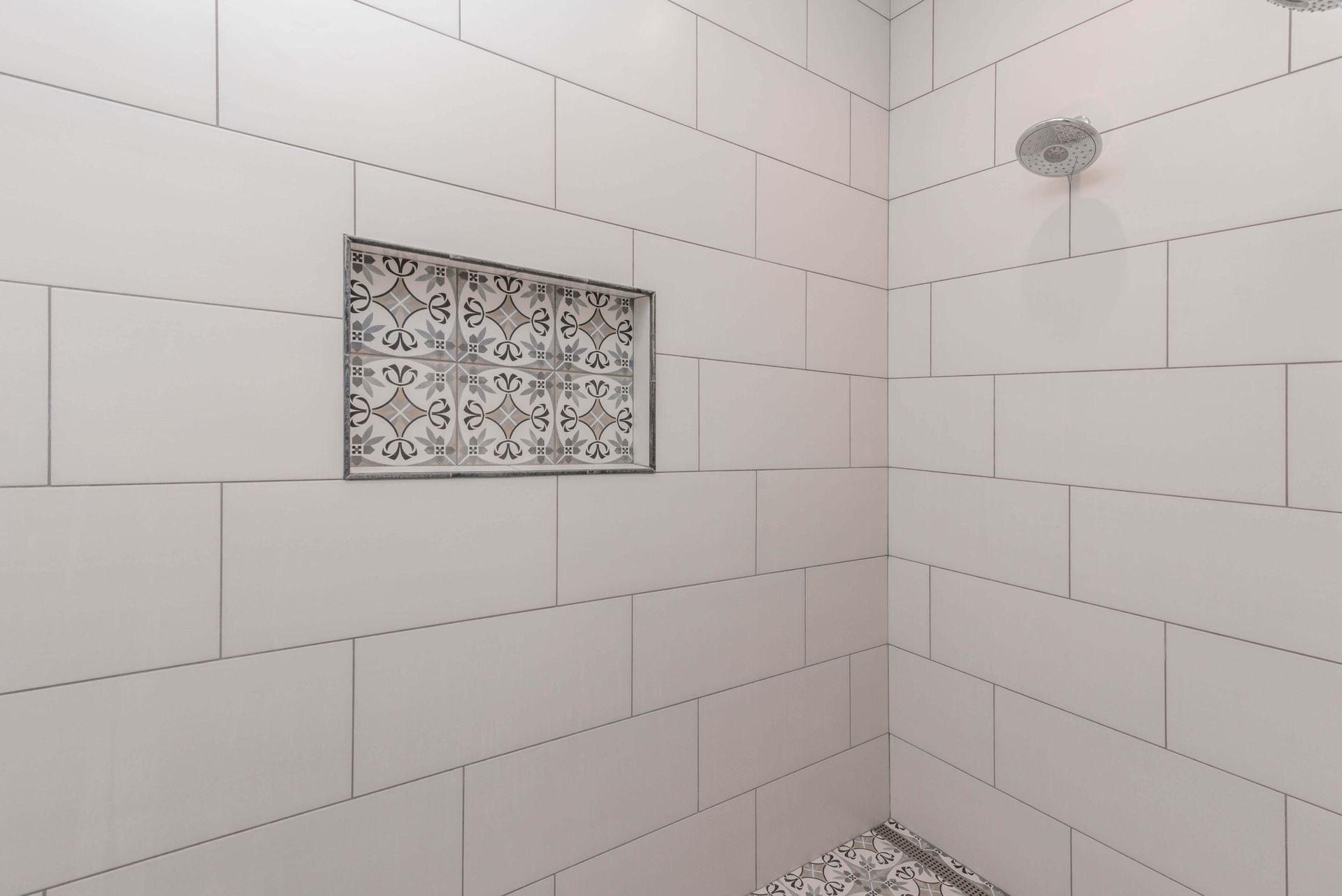 White tiled shower with patterned niche and pebble floor.