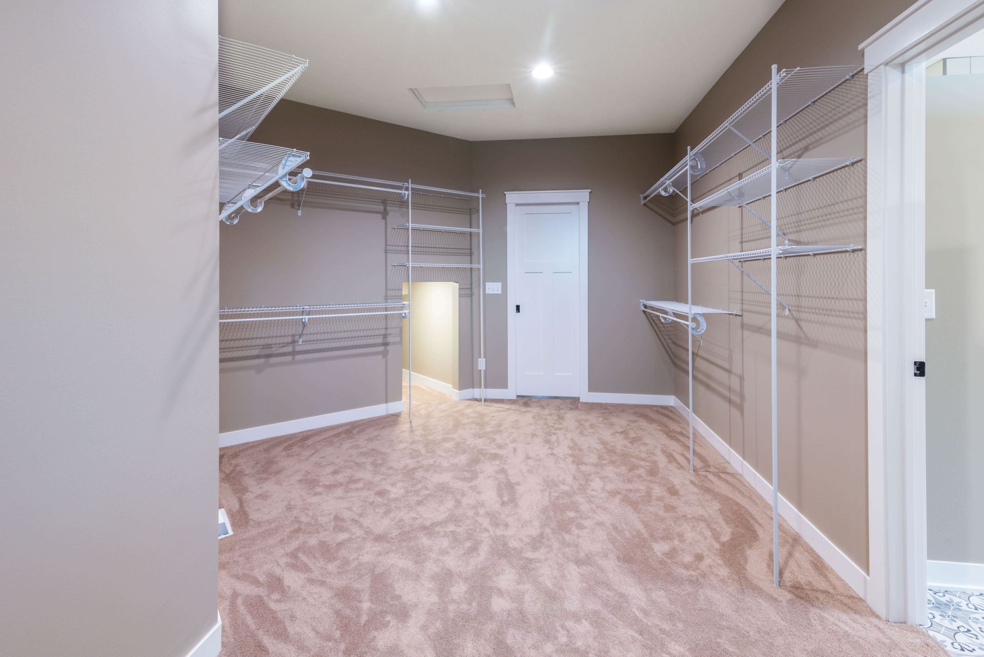 Empty walk-in closet with wire shelving and tan walls, tan carpet, and white door.