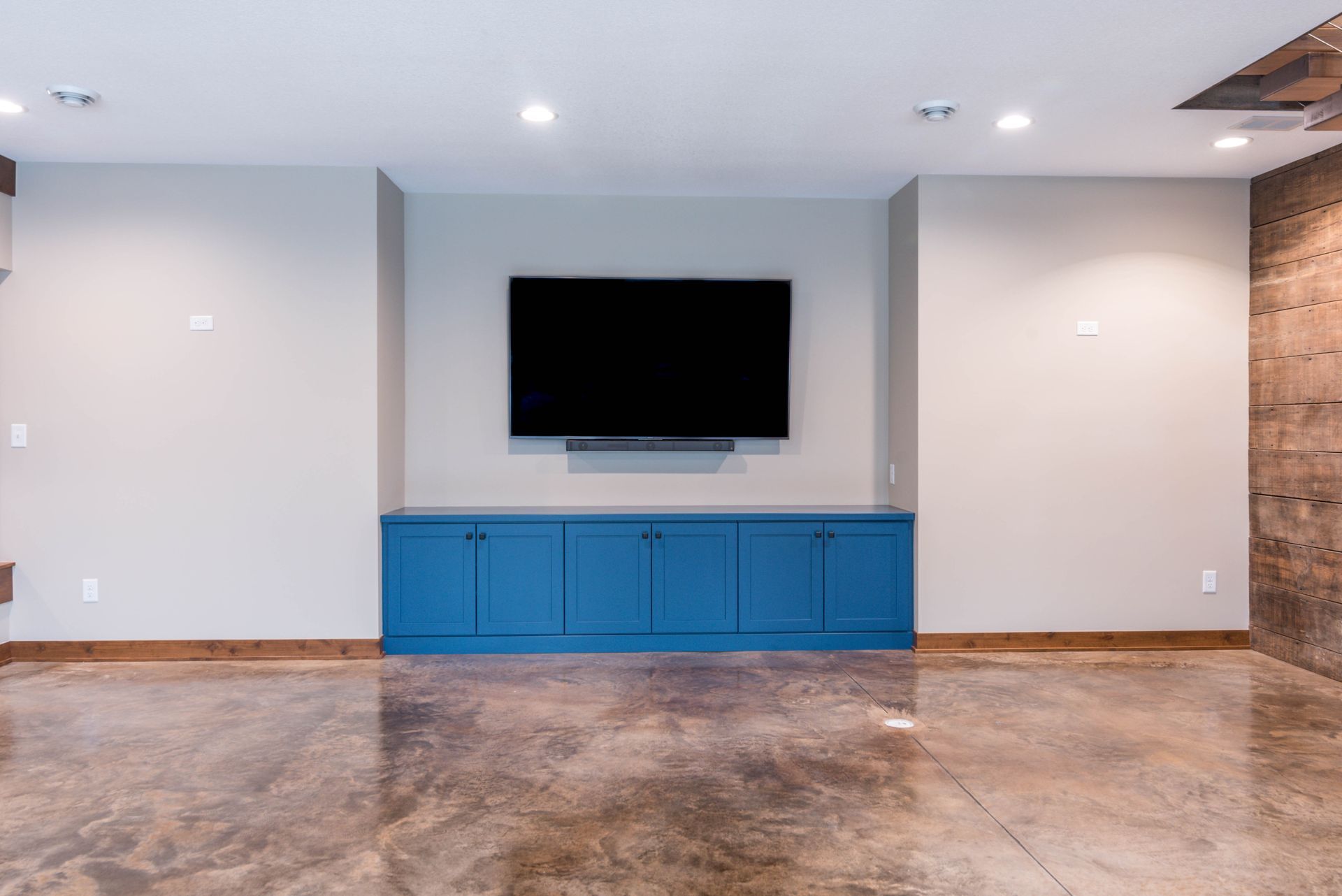 Living room with a large TV mounted above blue cabinets, polished concrete floor.