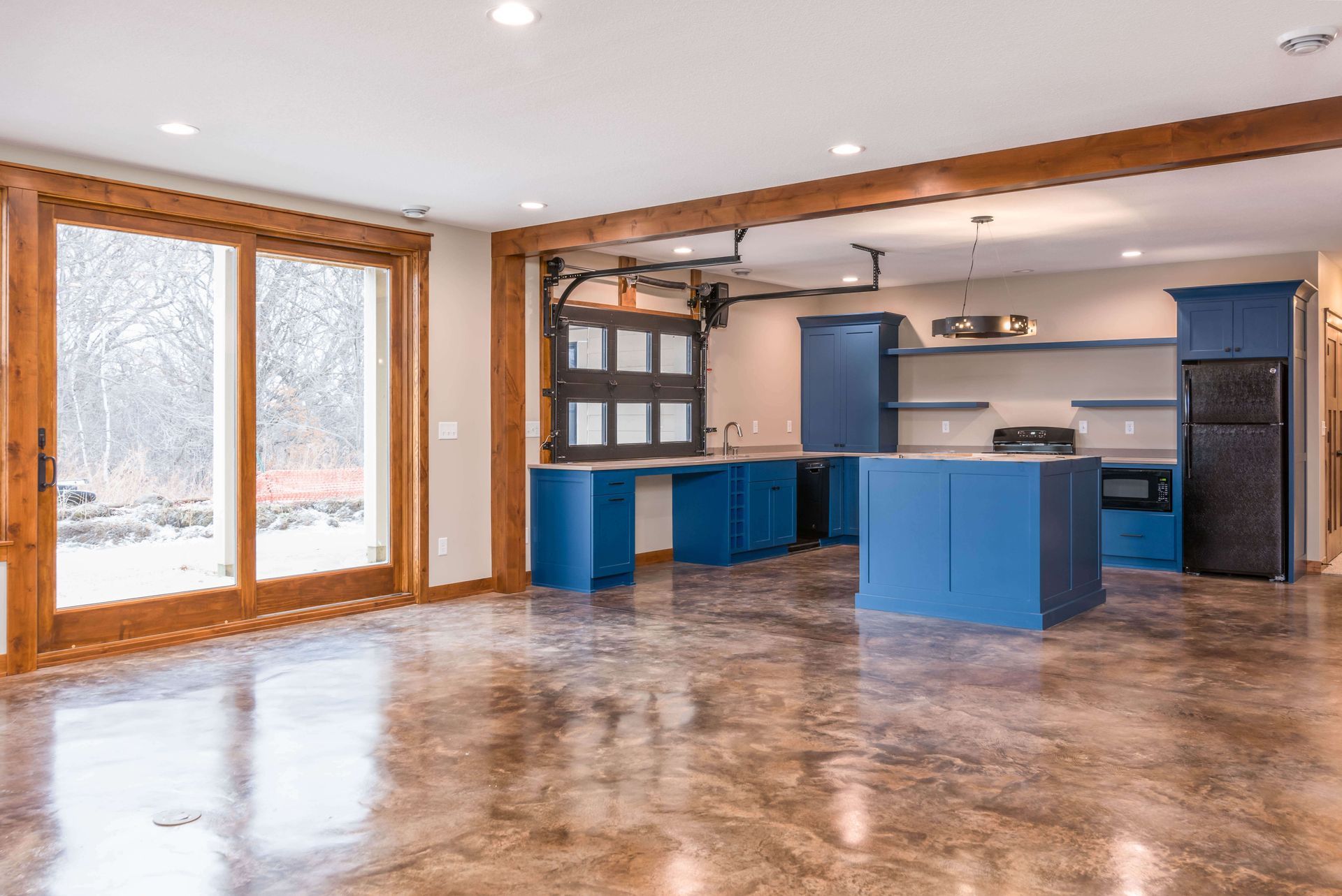 Open-concept kitchen with blue cabinets and a garage door backsplash, brown concrete floor.