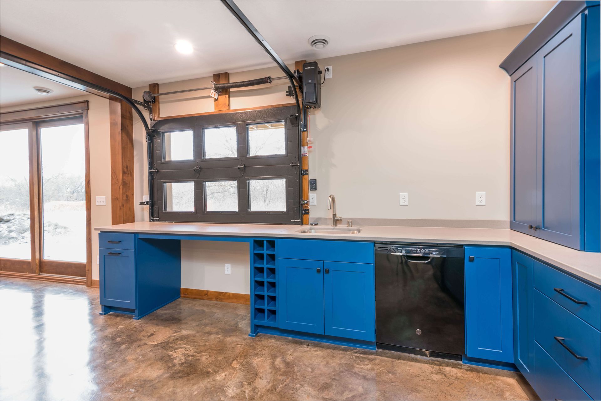 Blue kitchen with dark garage door window, built-in wine rack, and concrete floor.