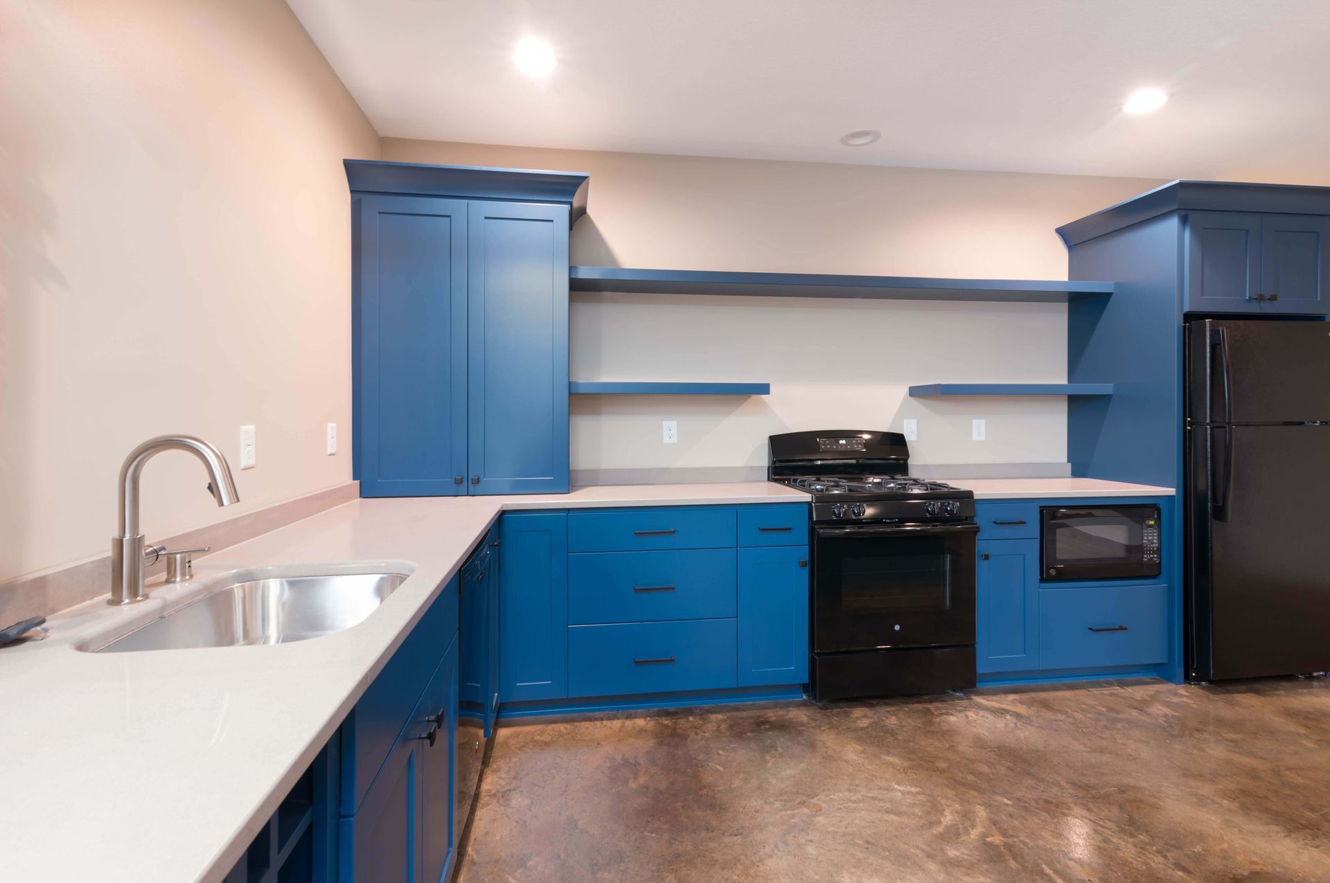 Blue kitchen cabinets, gray countertops, black appliances, and a stainless steel sink.
