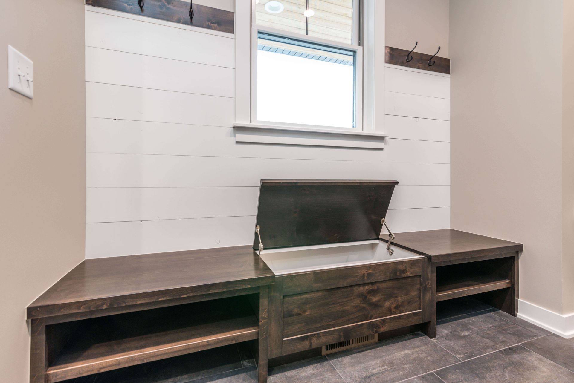 Dark wood bench with open storage and open shelving, against a white shiplap wall, under a window.