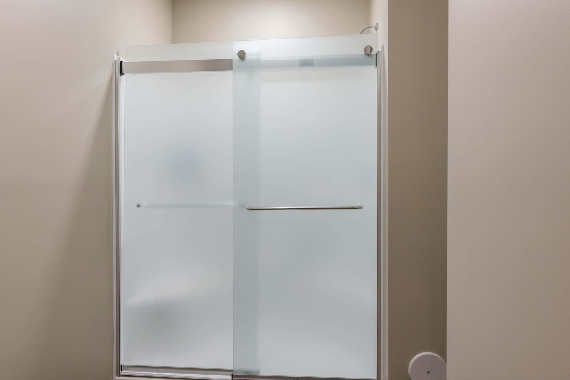 Frosted glass sliding shower doors in a bathroom with neutral-colored walls.