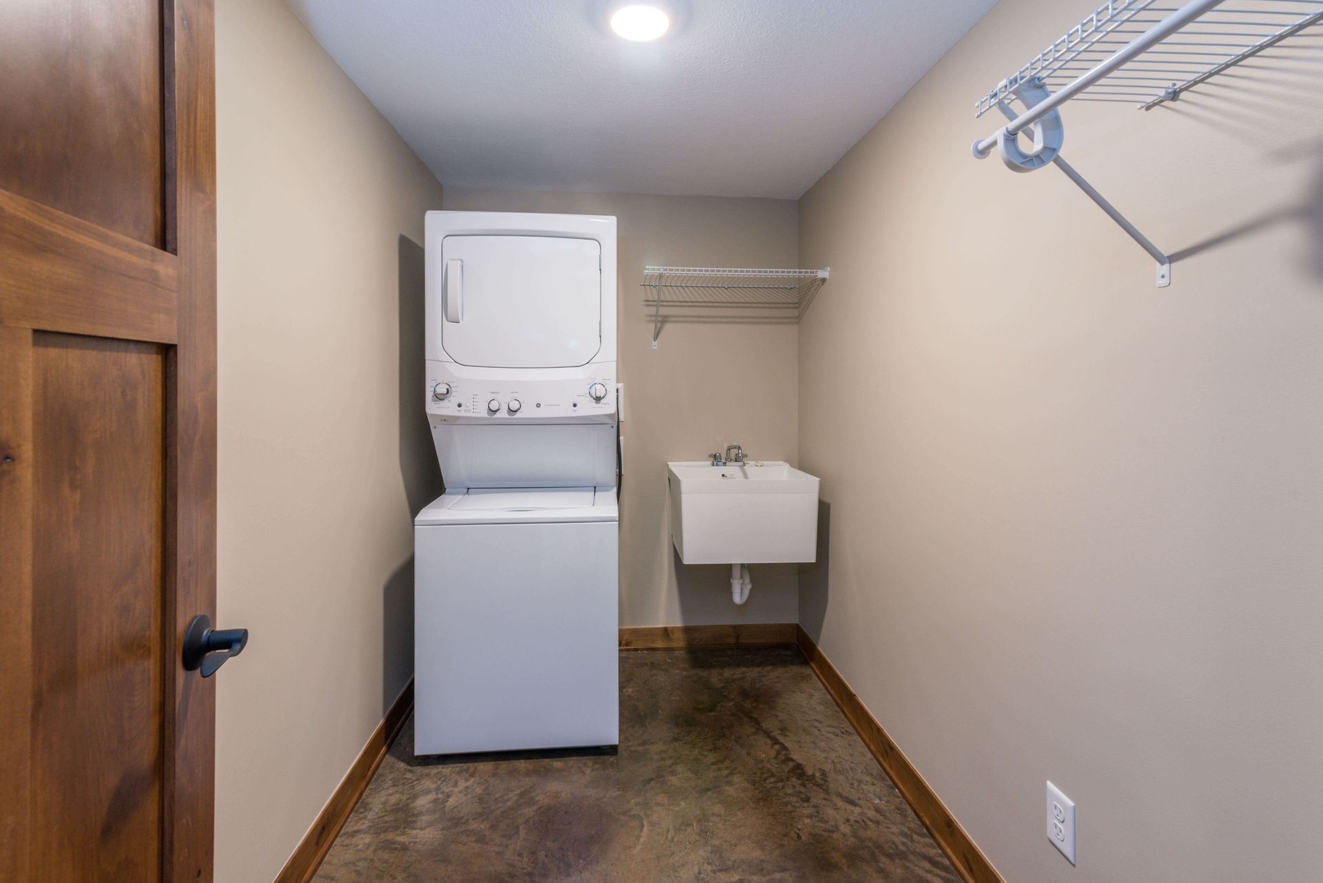 Laundry room with stacked washer and dryer, utility sink, and wire shelving.