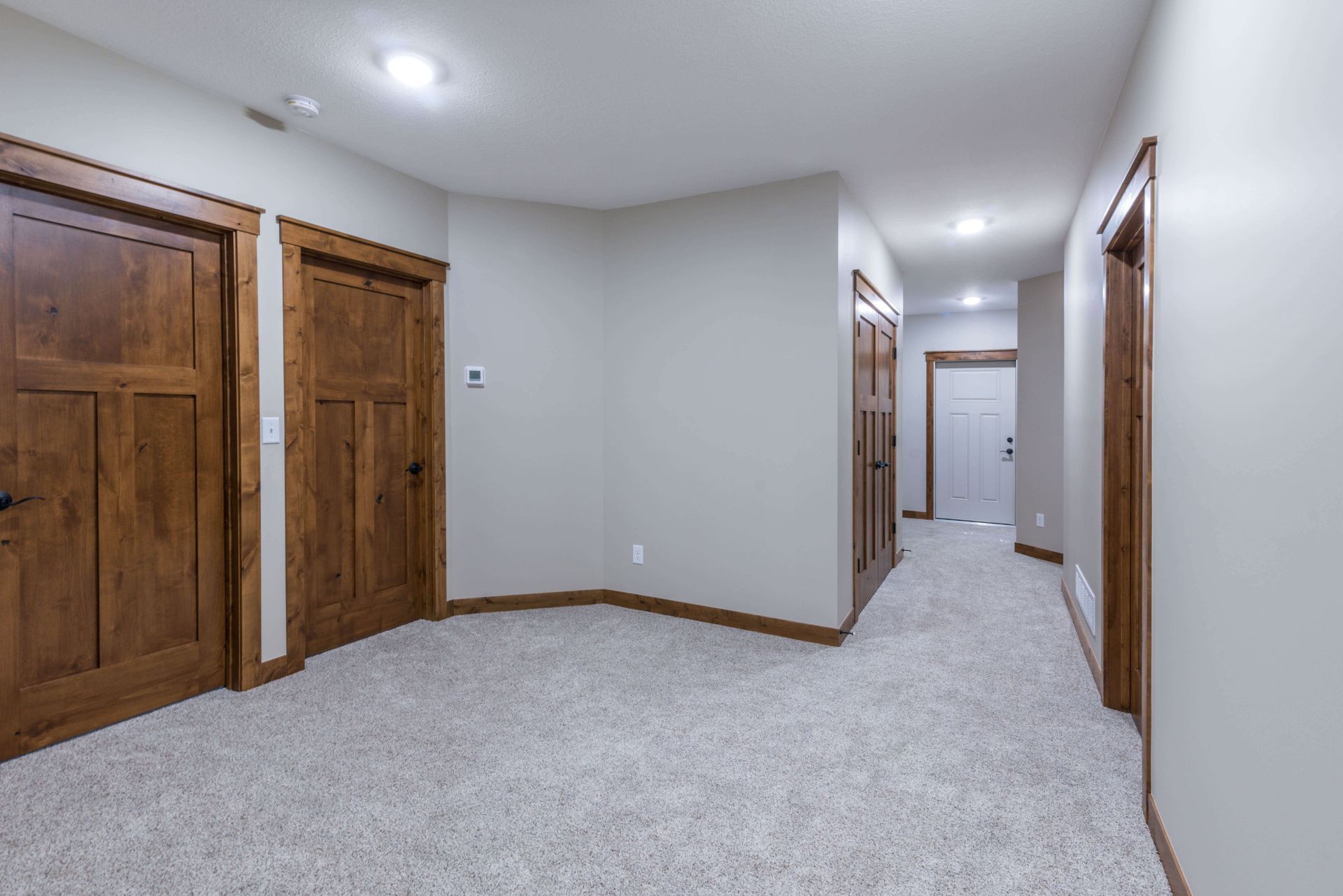 Hallway with carpet, light gray walls, brown doors and trim. Recessed ceiling lights.