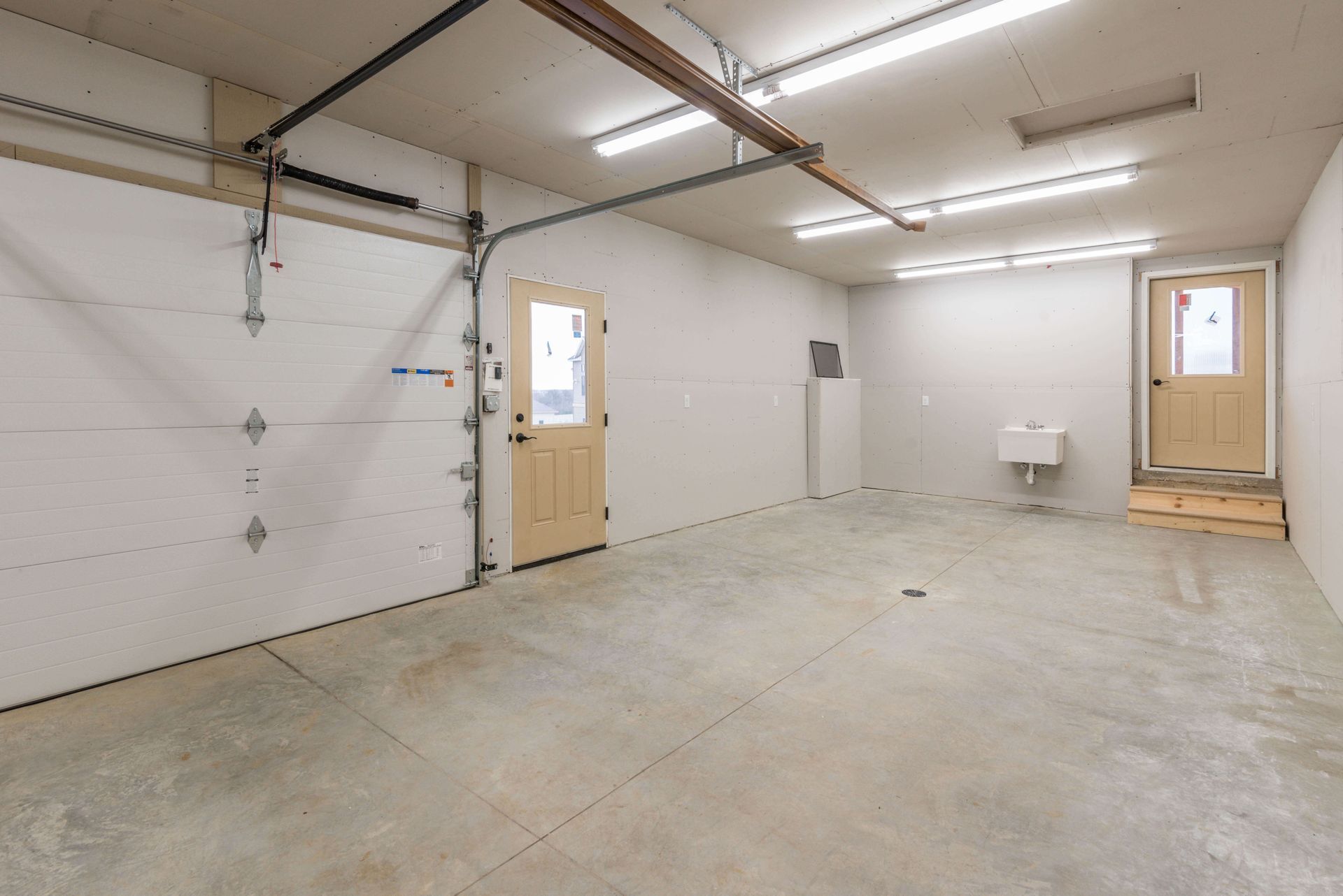 Empty garage interior with a concrete floor, garage door, and two entry doors.