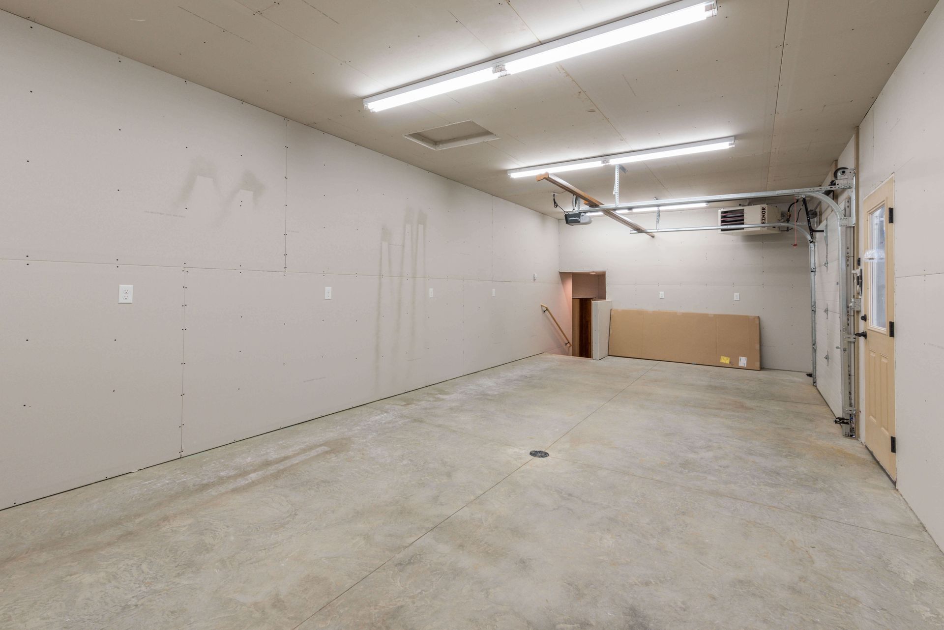 Empty garage with concrete floor, drywall walls, and overhead lighting.
