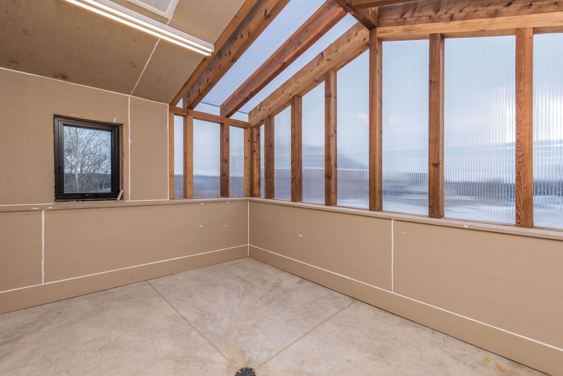 Interior of a sunroom with a transparent roof and walls, wooden beams, and a small window.