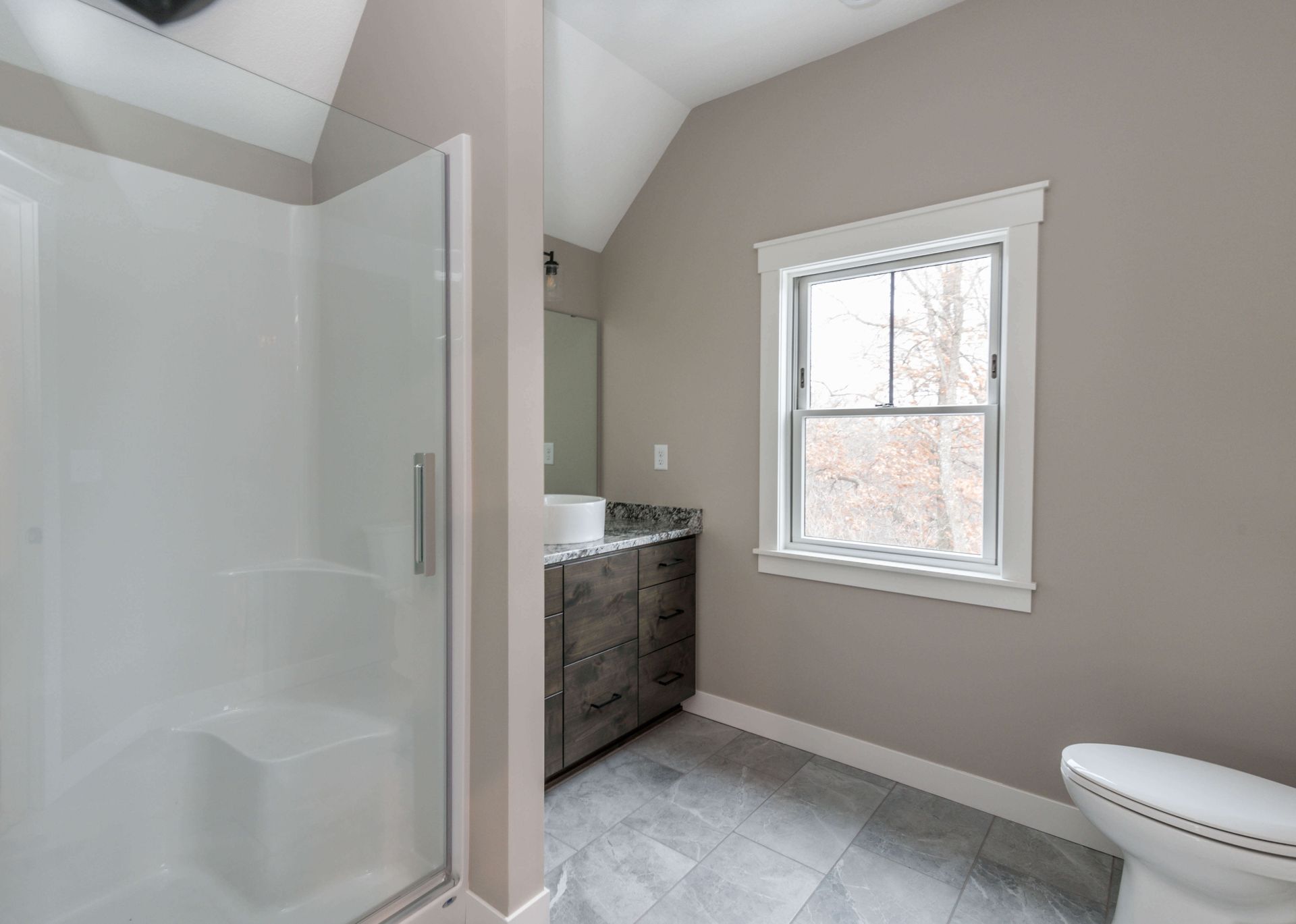 Bathroom with shower, vanity, toilet, and window. Gray walls, white trim, and gray tile floor.