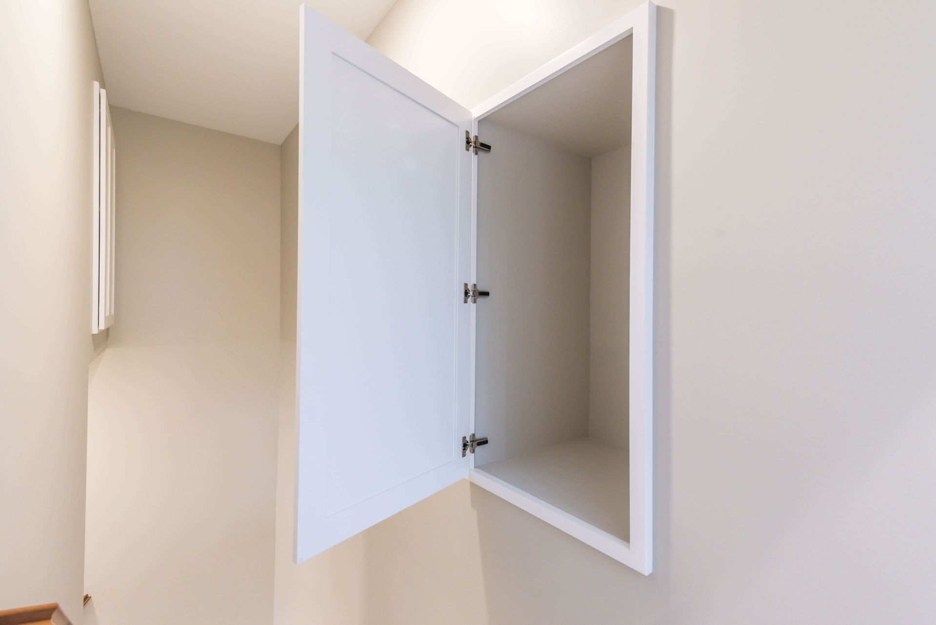 White cabinet with open door on a beige wall, next to a hallway.