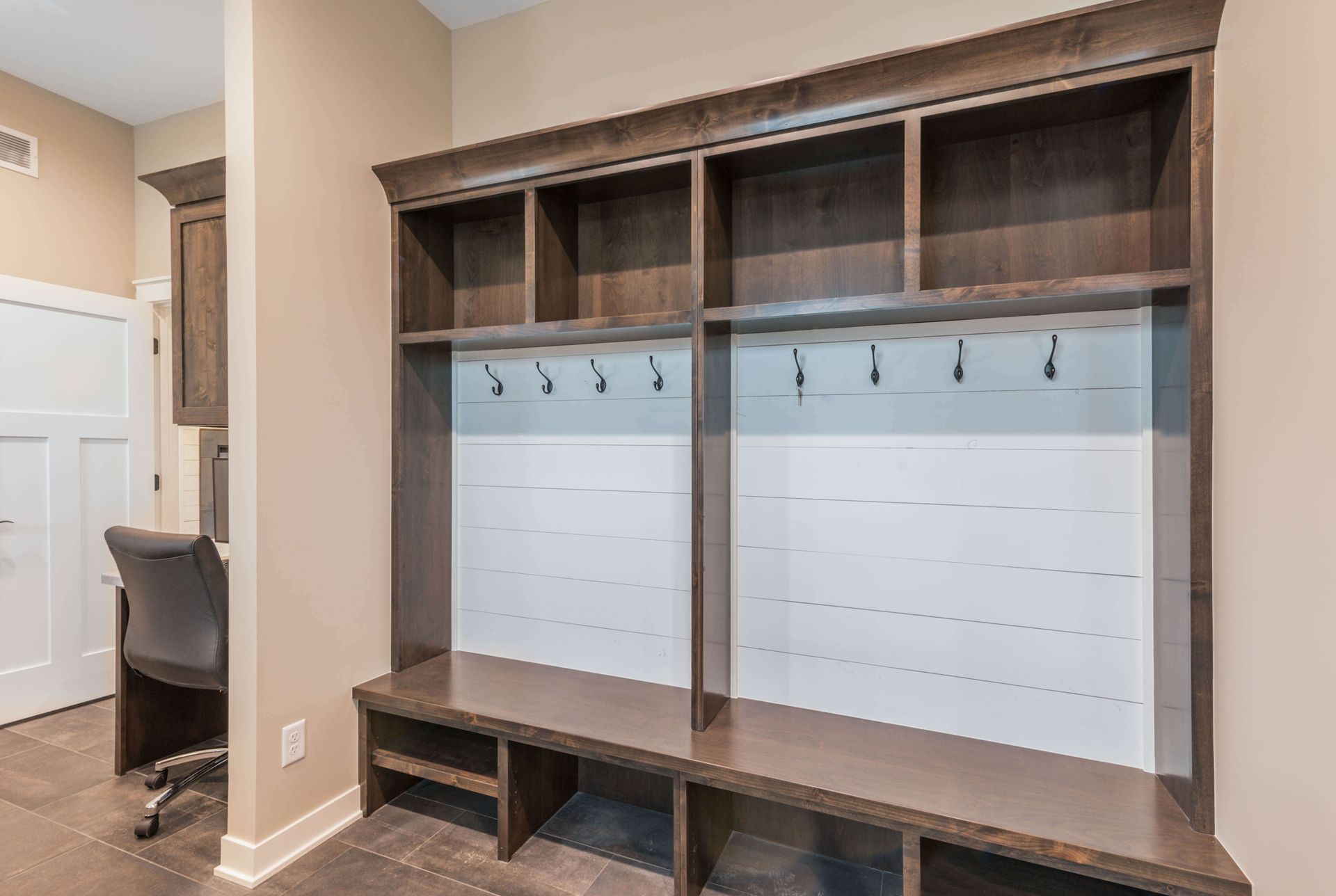 Dark wood entryway storage with cubbies, hooks, and bench, in a beige room.