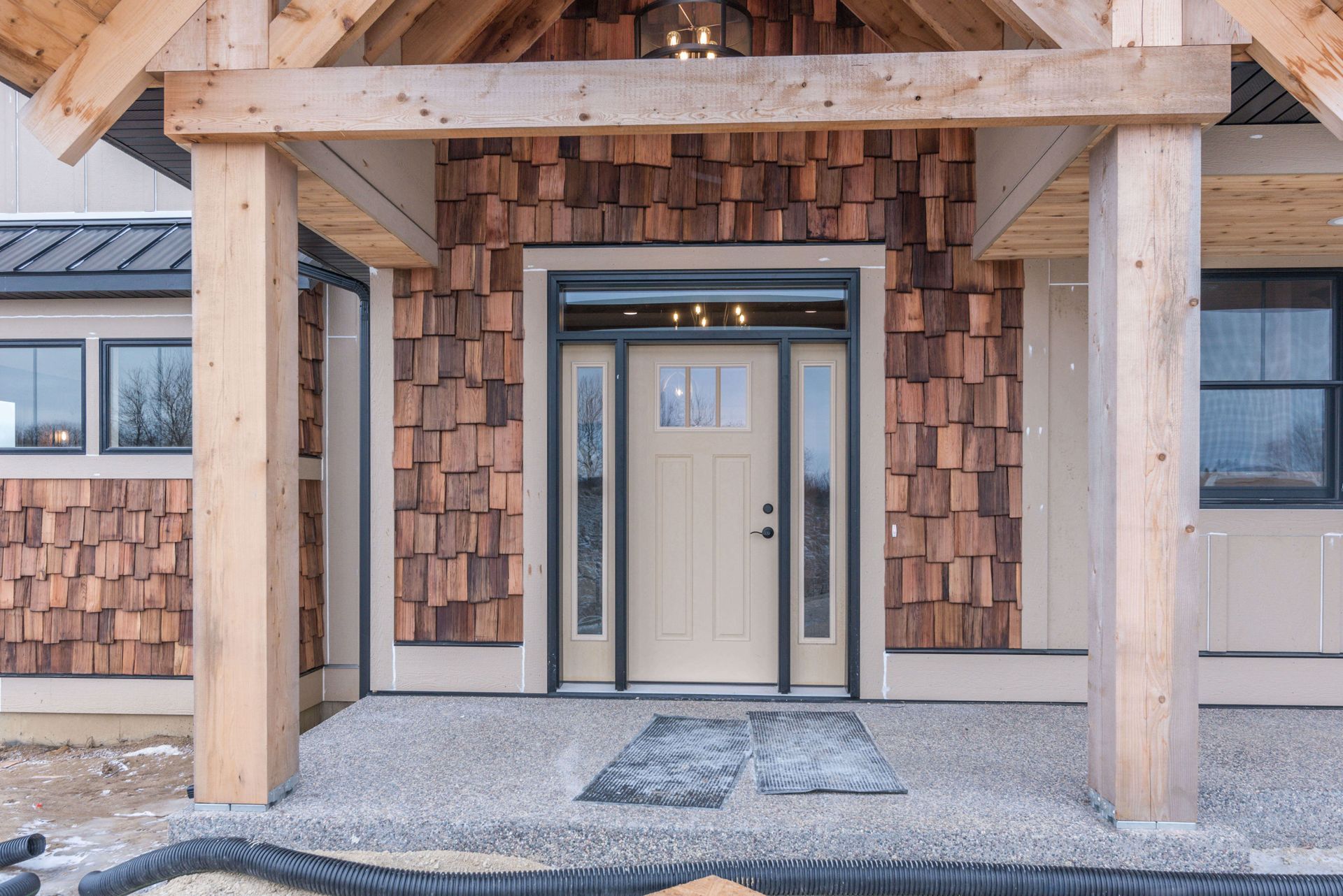 Beige front door with sidelights, under a wooden porch roof, and cedar shingle siding.