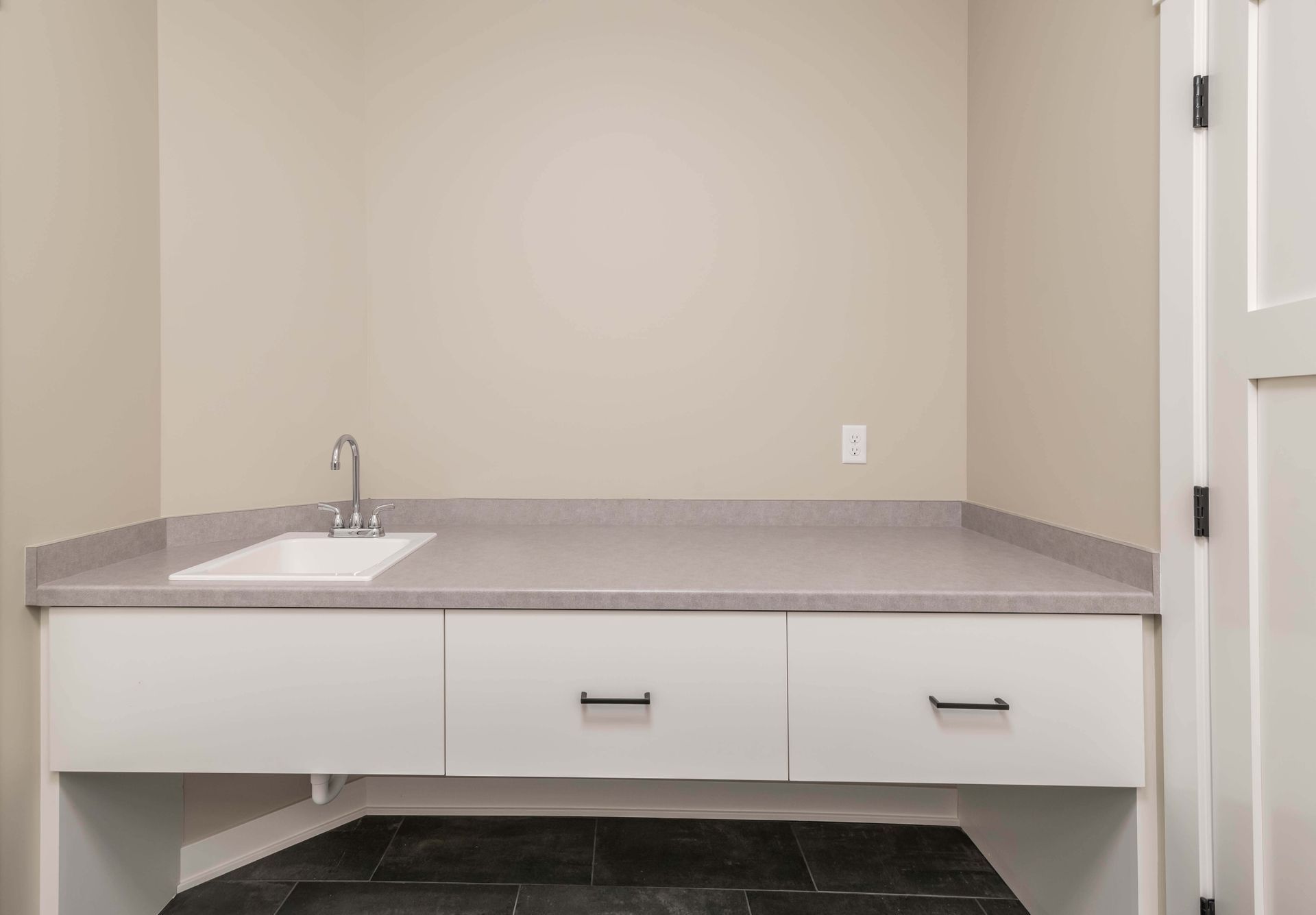 White laundry room with sink, countertop, cabinets, and dark tile floor.