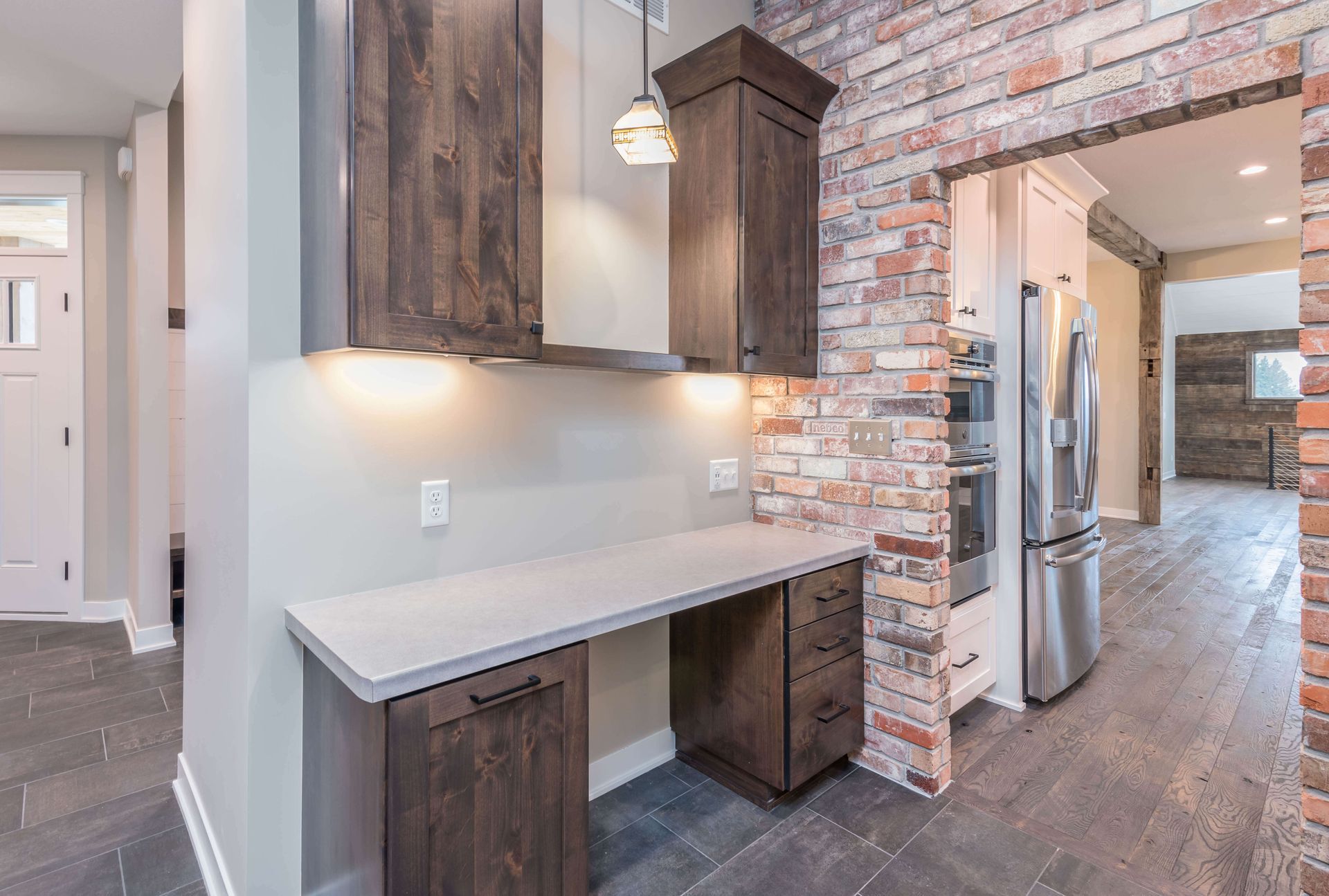 Built-in desk with dark wood cabinets, brick accent wall, and tiled floor.