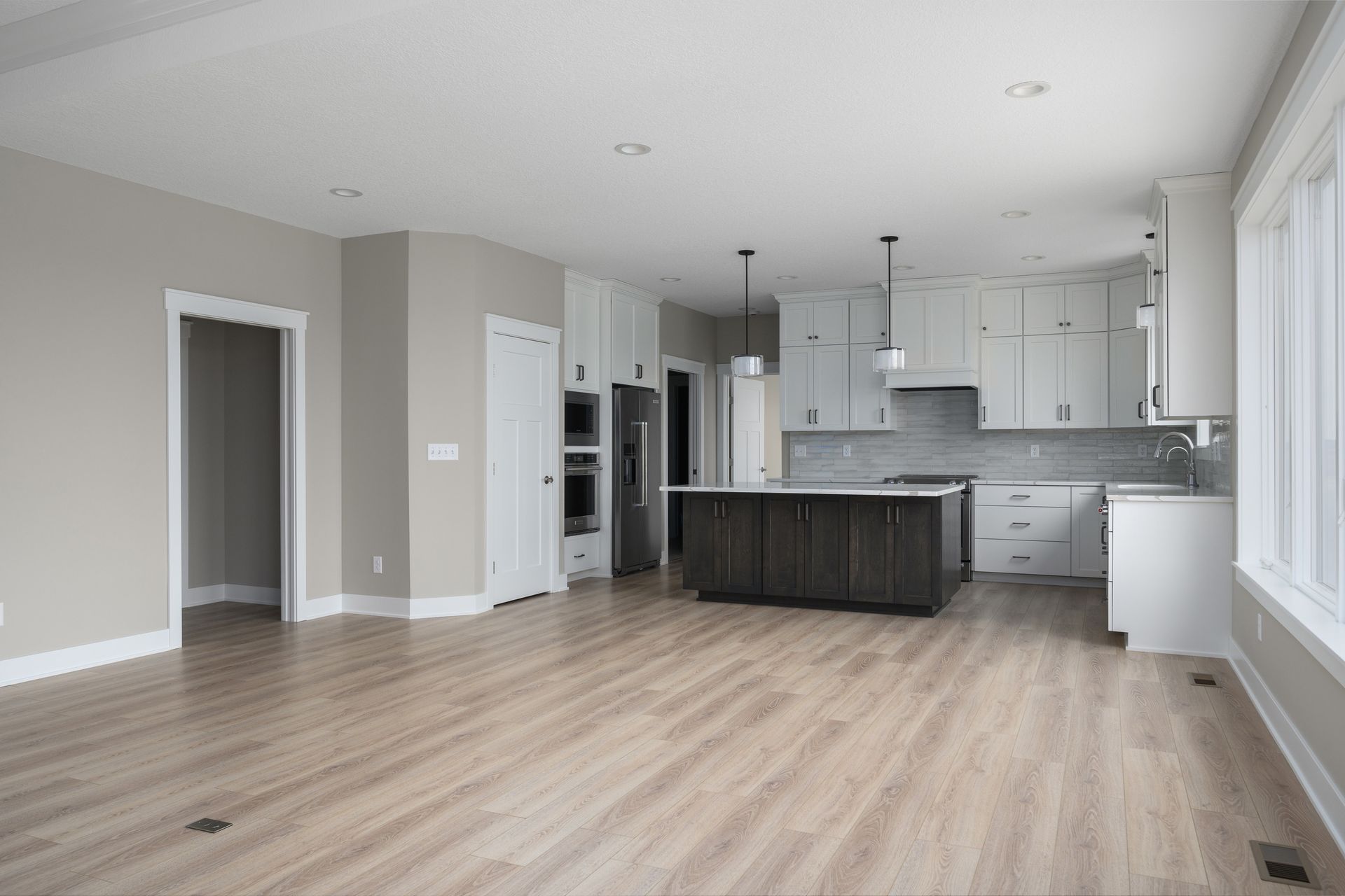 Open-concept kitchen and living area with wood floors, white cabinetry, dark island, and large windows.