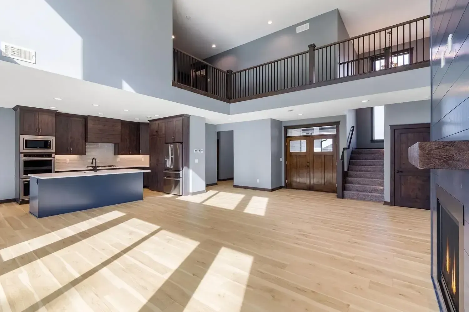 Open-concept kitchen and living area with a loft. Features wood floors, blue island, and dark wood cabinetry.