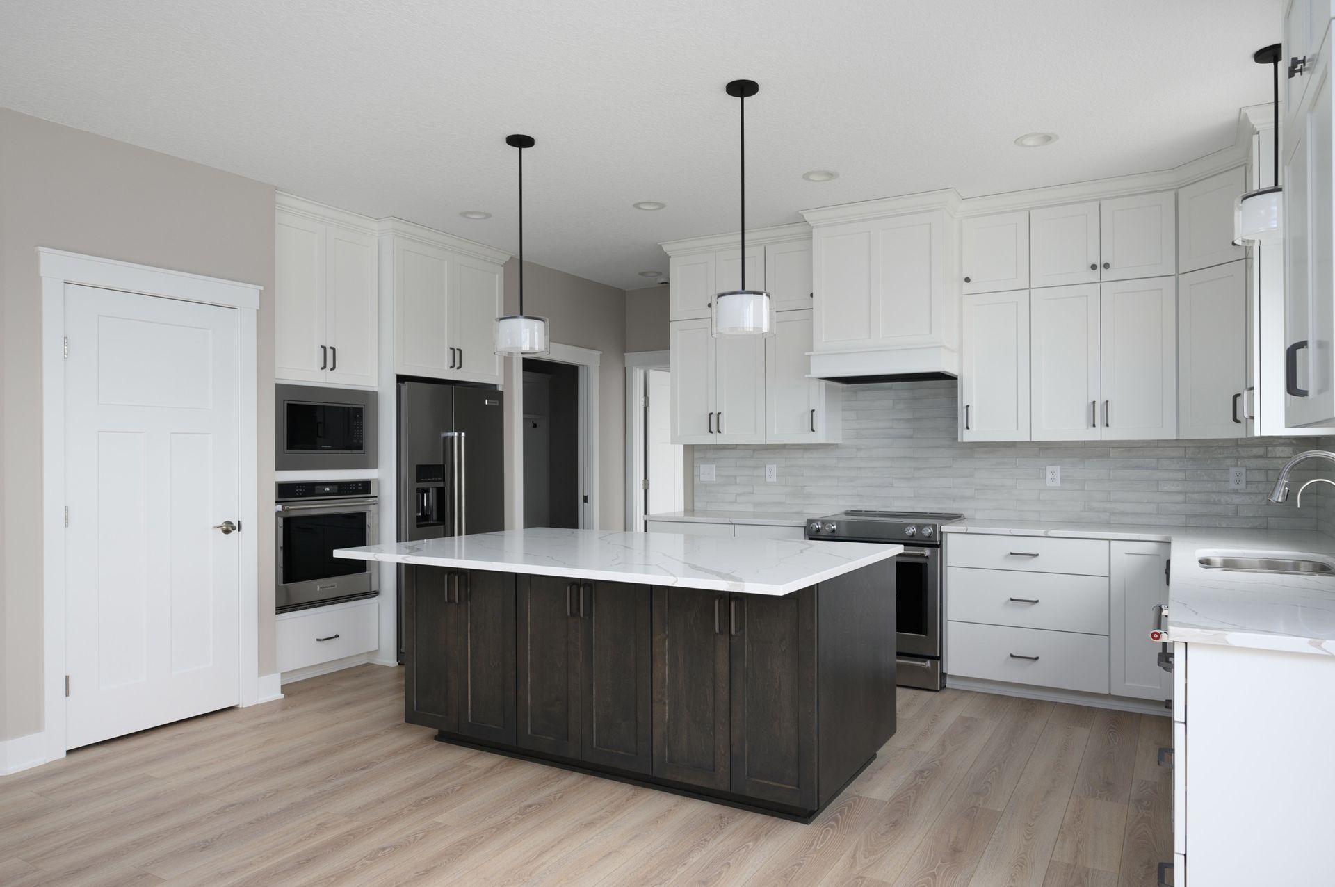 Modern kitchen with white cabinets, dark island, stainless appliances, and wood floors.