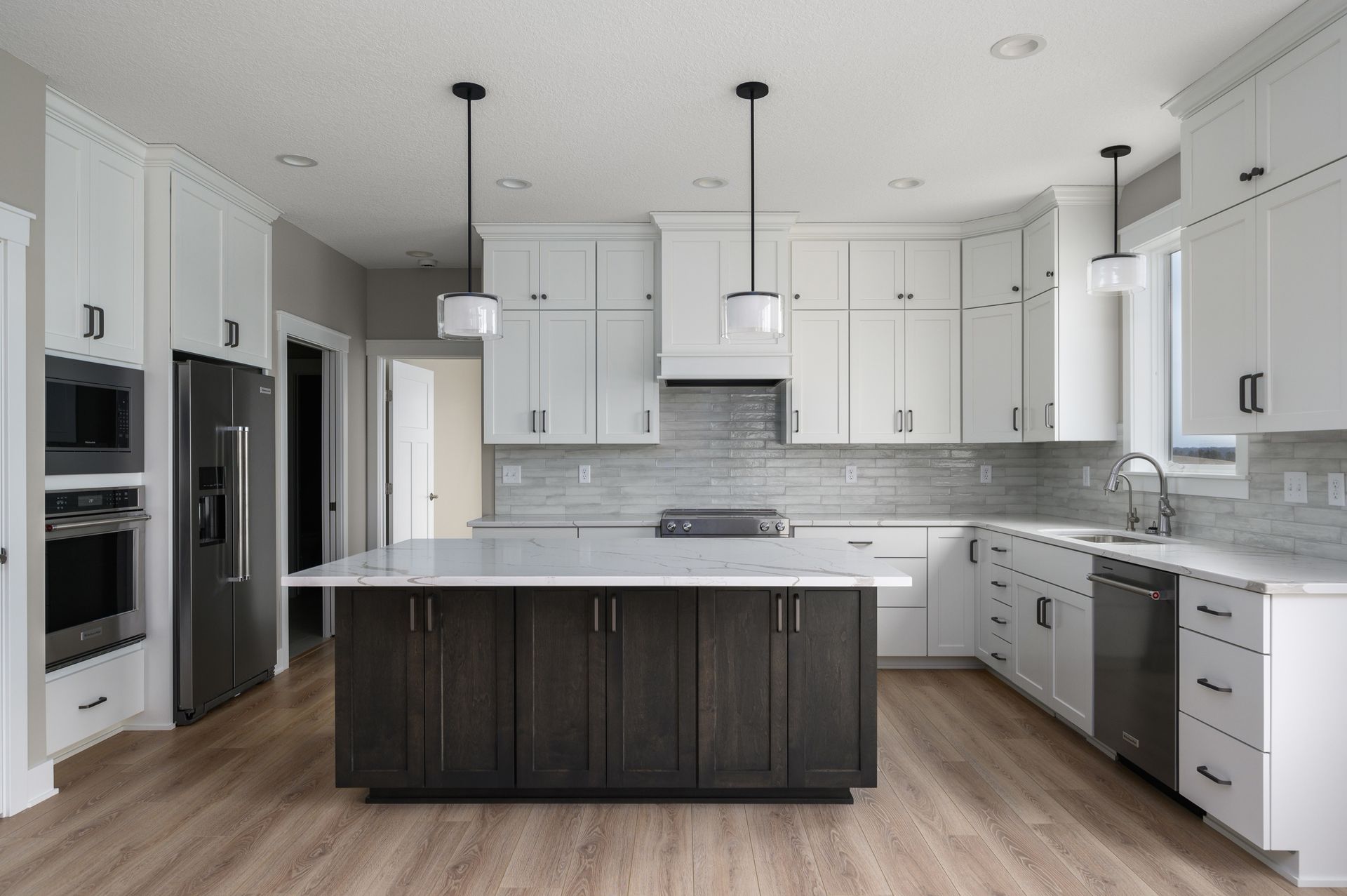 Modern kitchen with white upper cabinets, dark island, stainless steel appliances, and wood floors.