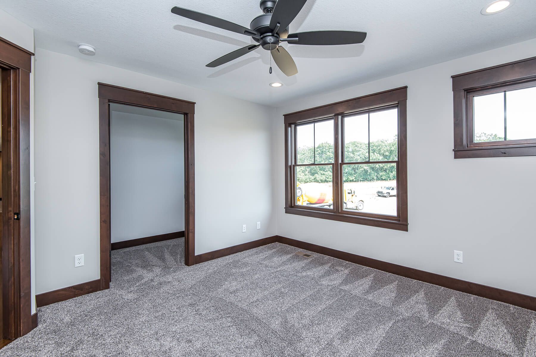 Empty bedroom with gray carpet, brown trim, and a ceiling fan.