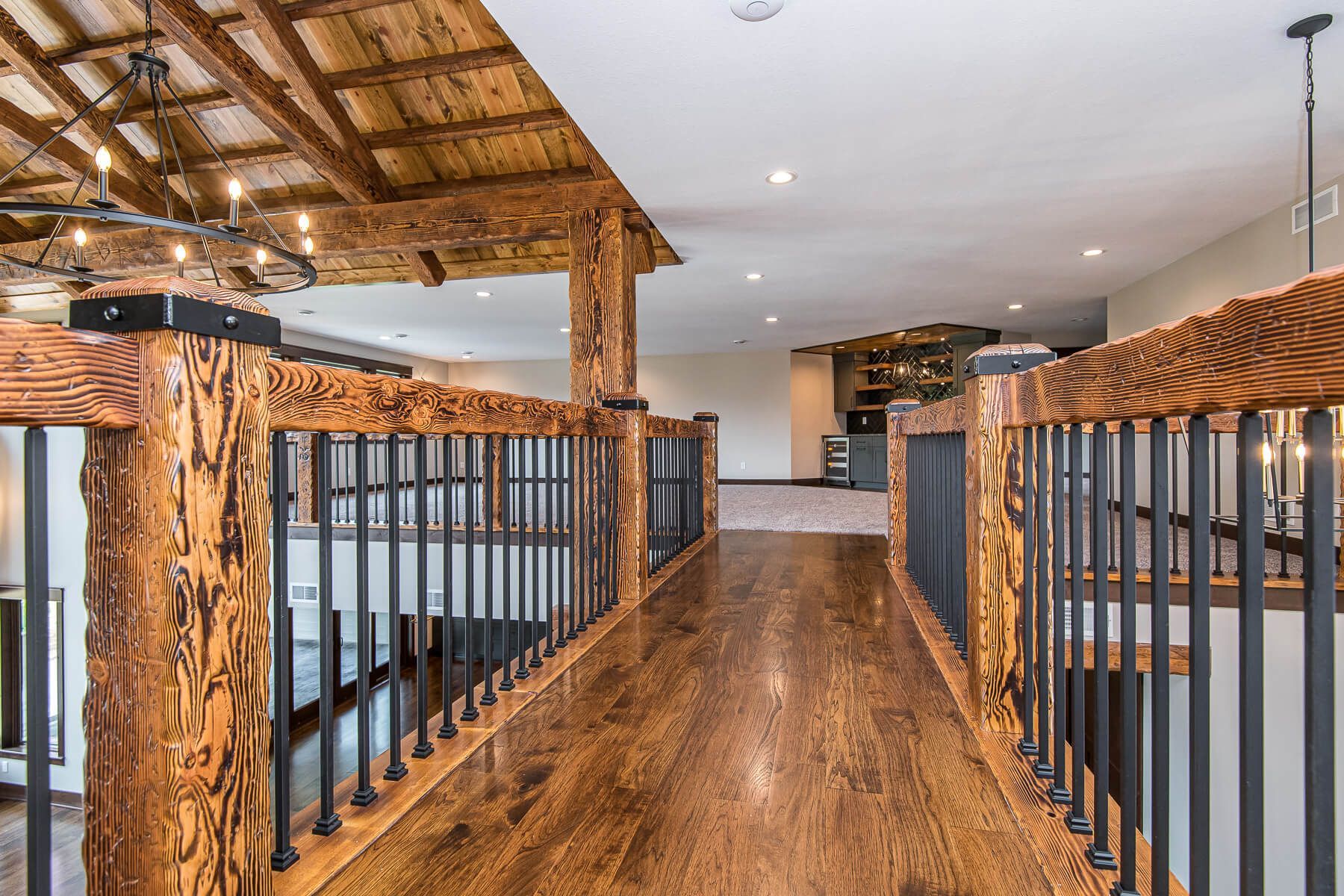Wooden hallway with log-style railing and ceiling beams, leading toward a lit living area.