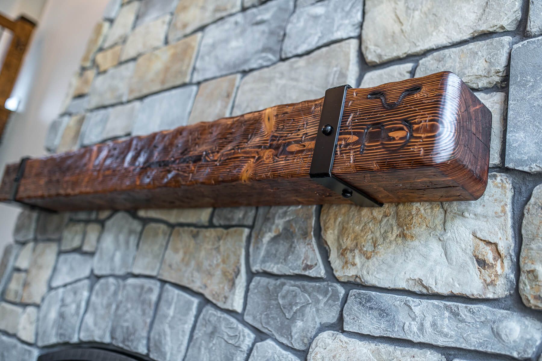 Wooden mantel with dark metal brackets on a stone fireplace.
