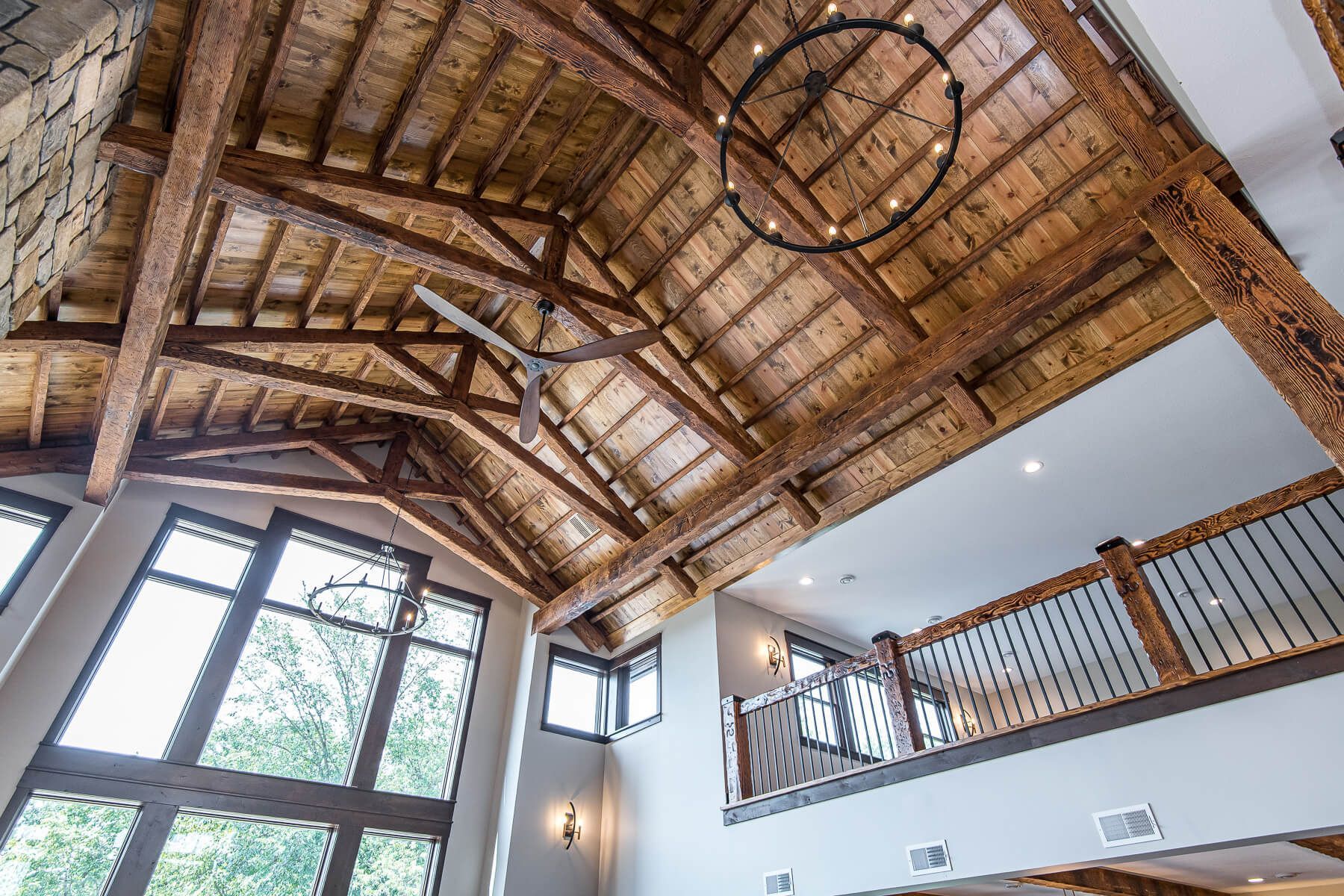 Wooden beams and ceiling in a high-ceilinged room with windows and a balcony. A circular chandelier hangs.