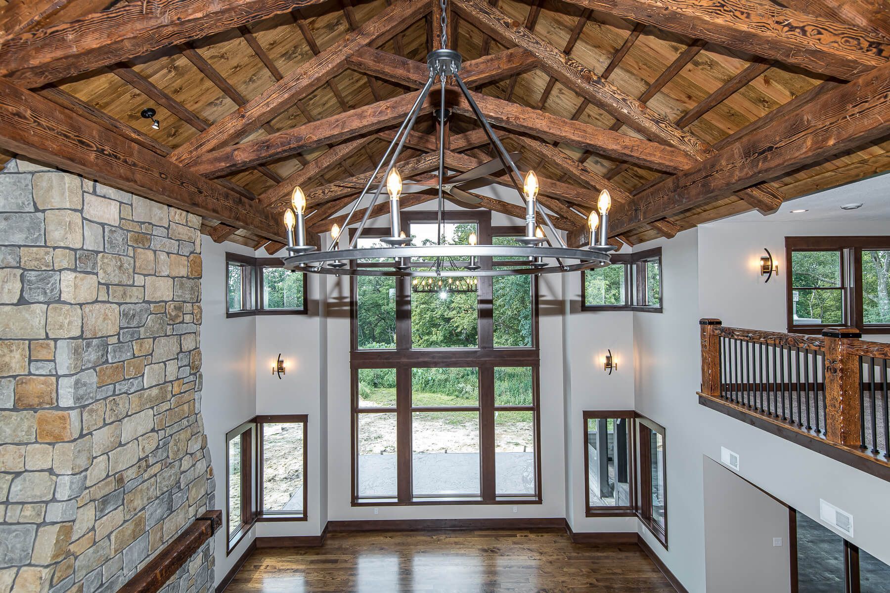 High-ceilinged entry with stone wall, wooden beams, large windows, and a chandelier.