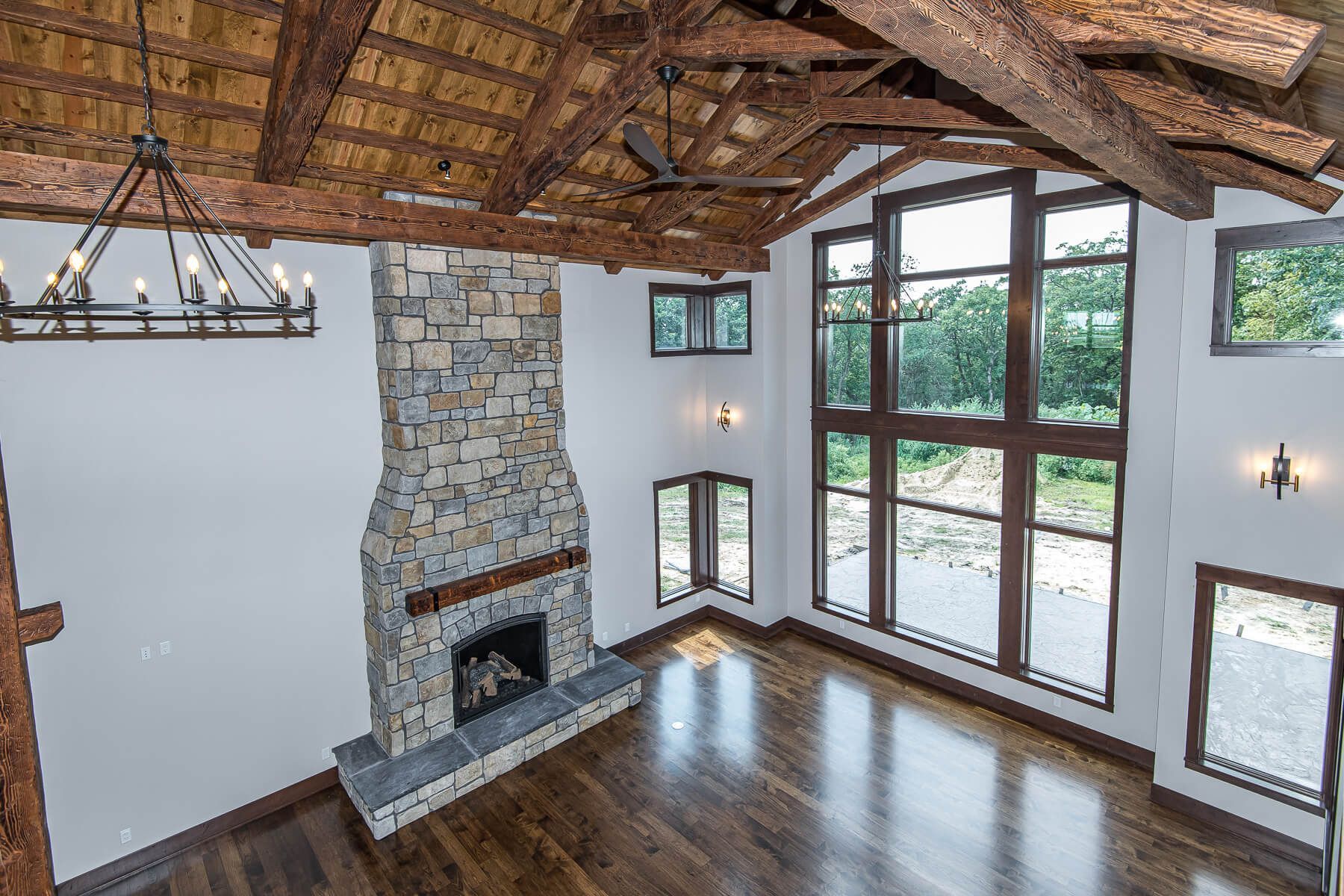 High-ceiling living room with stone fireplace, dark wood floors, and large windows.