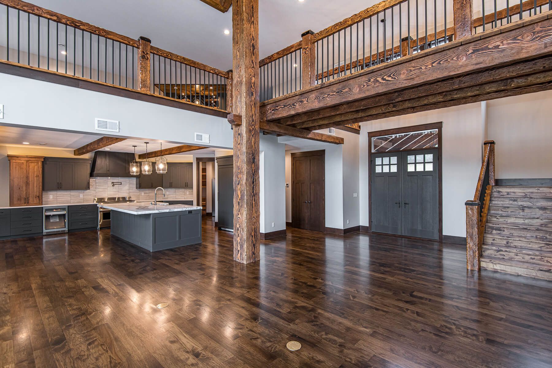 Spacious interior with exposed wooden beams, a loft, dark cabinets, and hardwood floors.