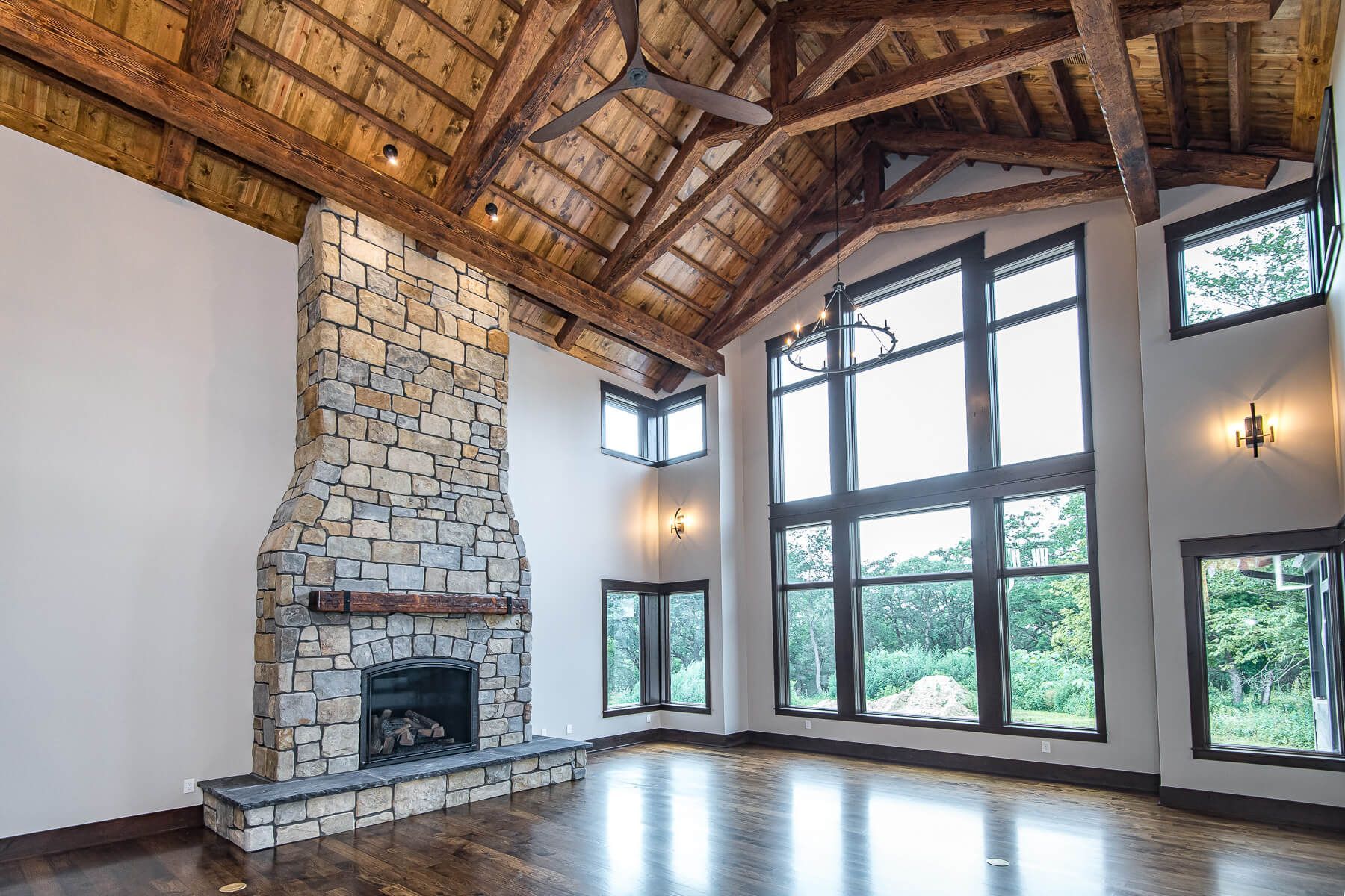 Spacious room with stone fireplace, wooden beams, large windows, and hardwood floors.