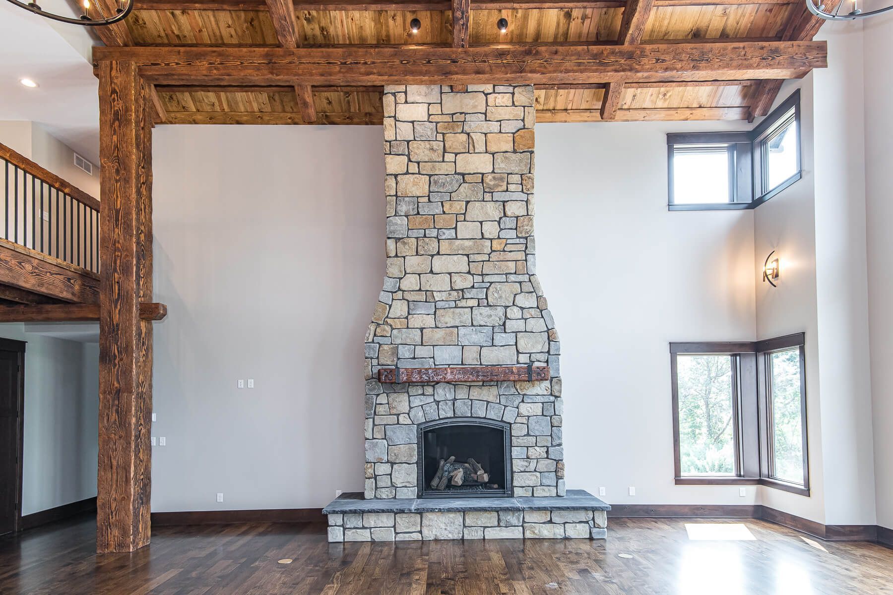 Stone fireplace in a modern living room with exposed wood beams and hardwood floors.