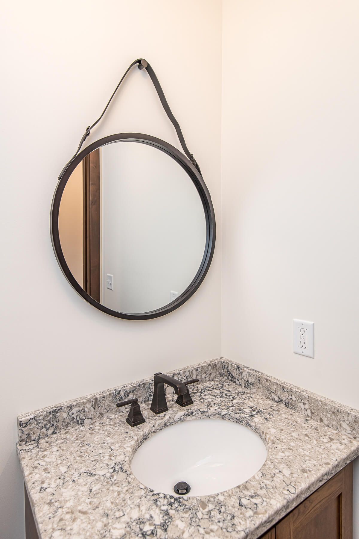 Bathroom with round mirror, granite countertop, and dark faucet.
