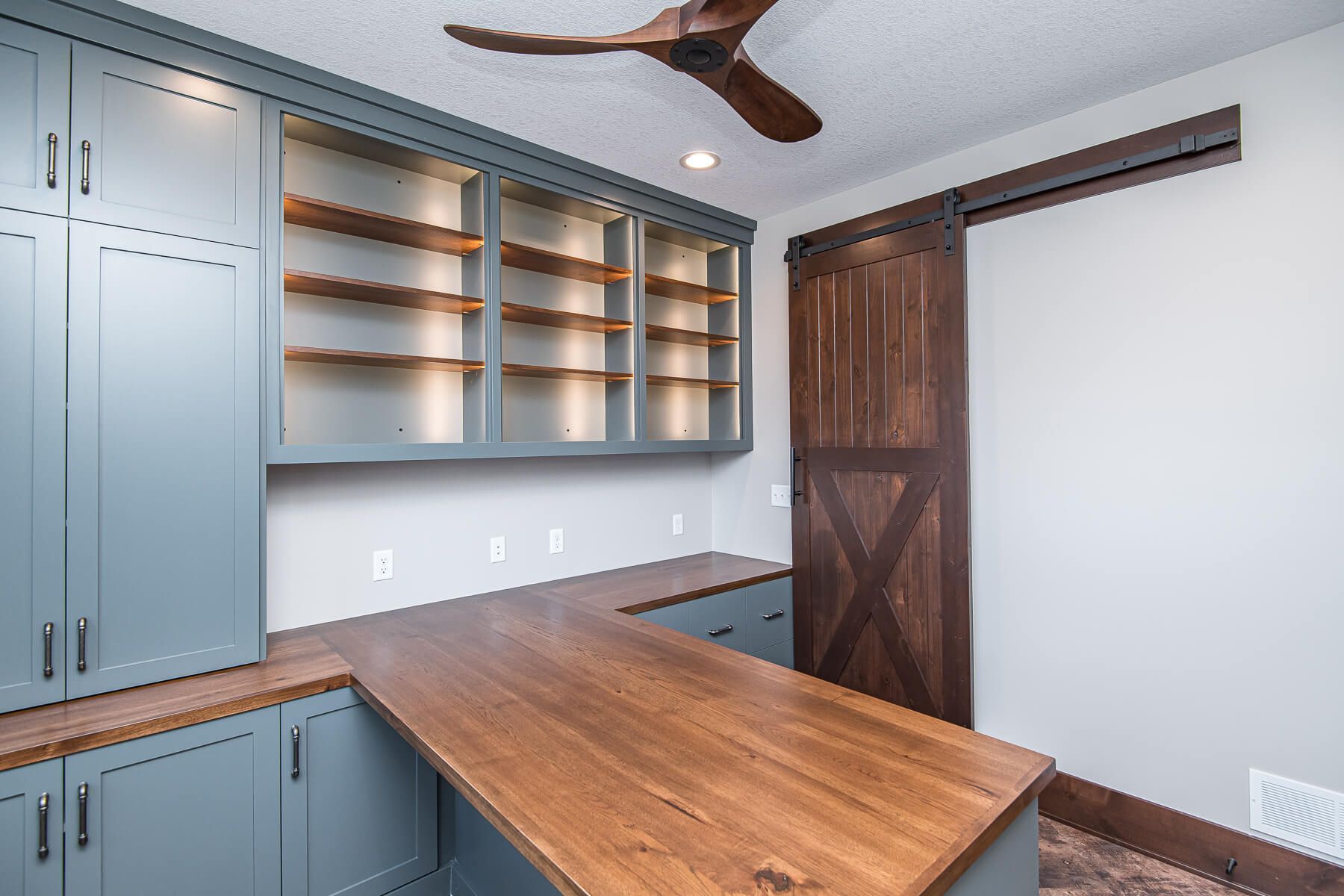 Home office with blue cabinets, wooden desk, and a sliding barn door.