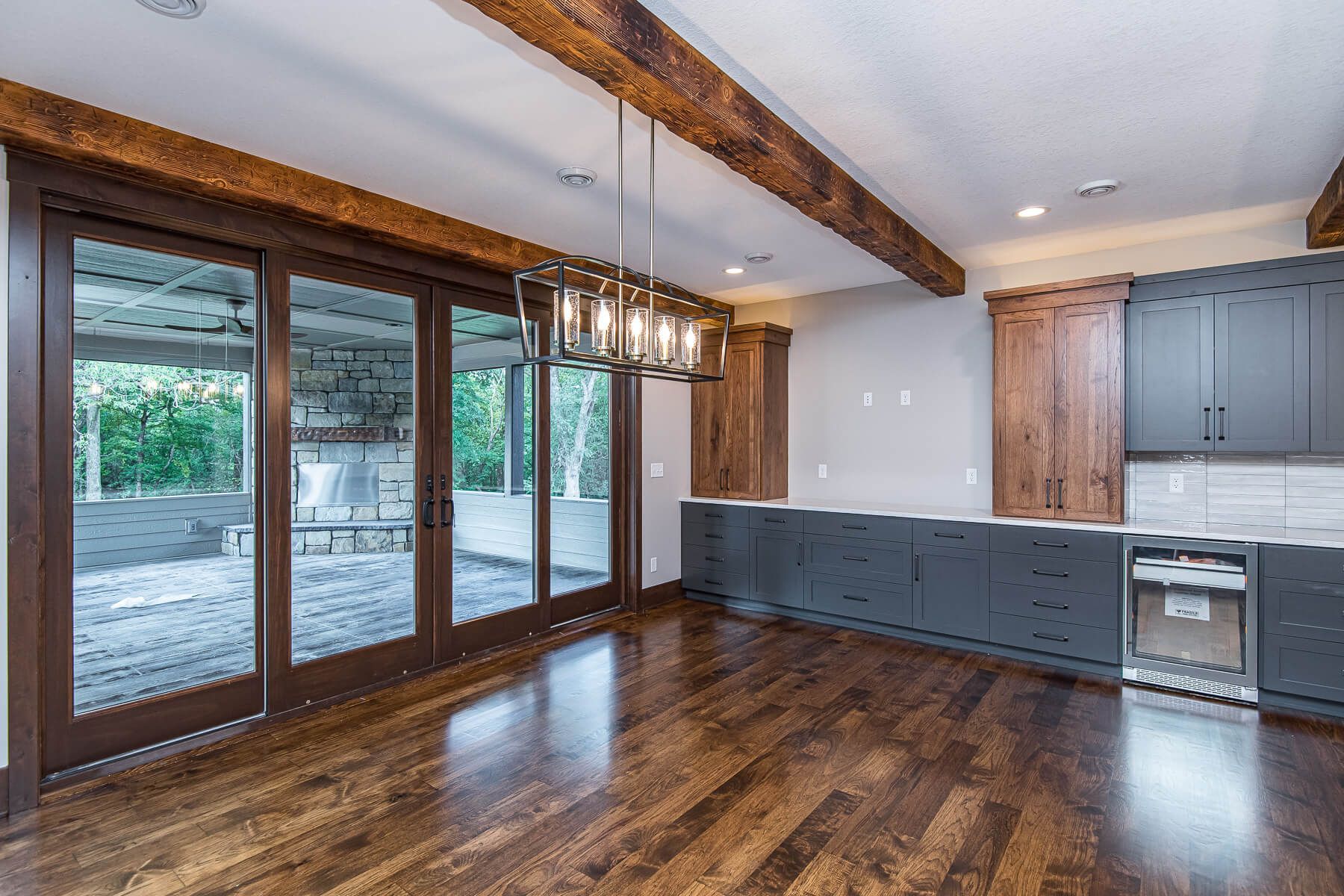 Dining room with dark wood floors, cabinets, and beams. Large sliding glass doors lead to a patio.