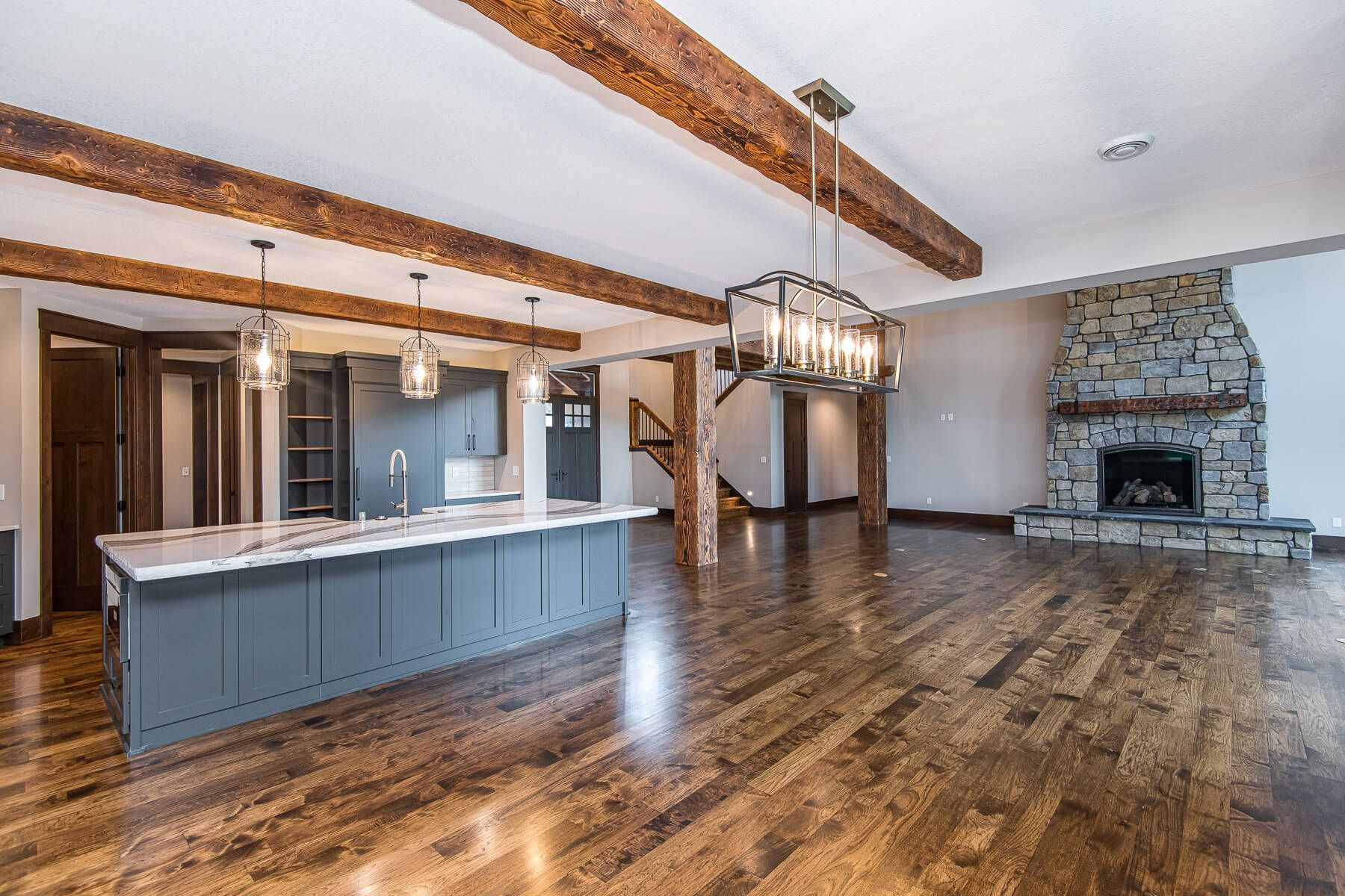 Open-concept kitchen and living area with wood beams, stone fireplace, and hardwood floors.