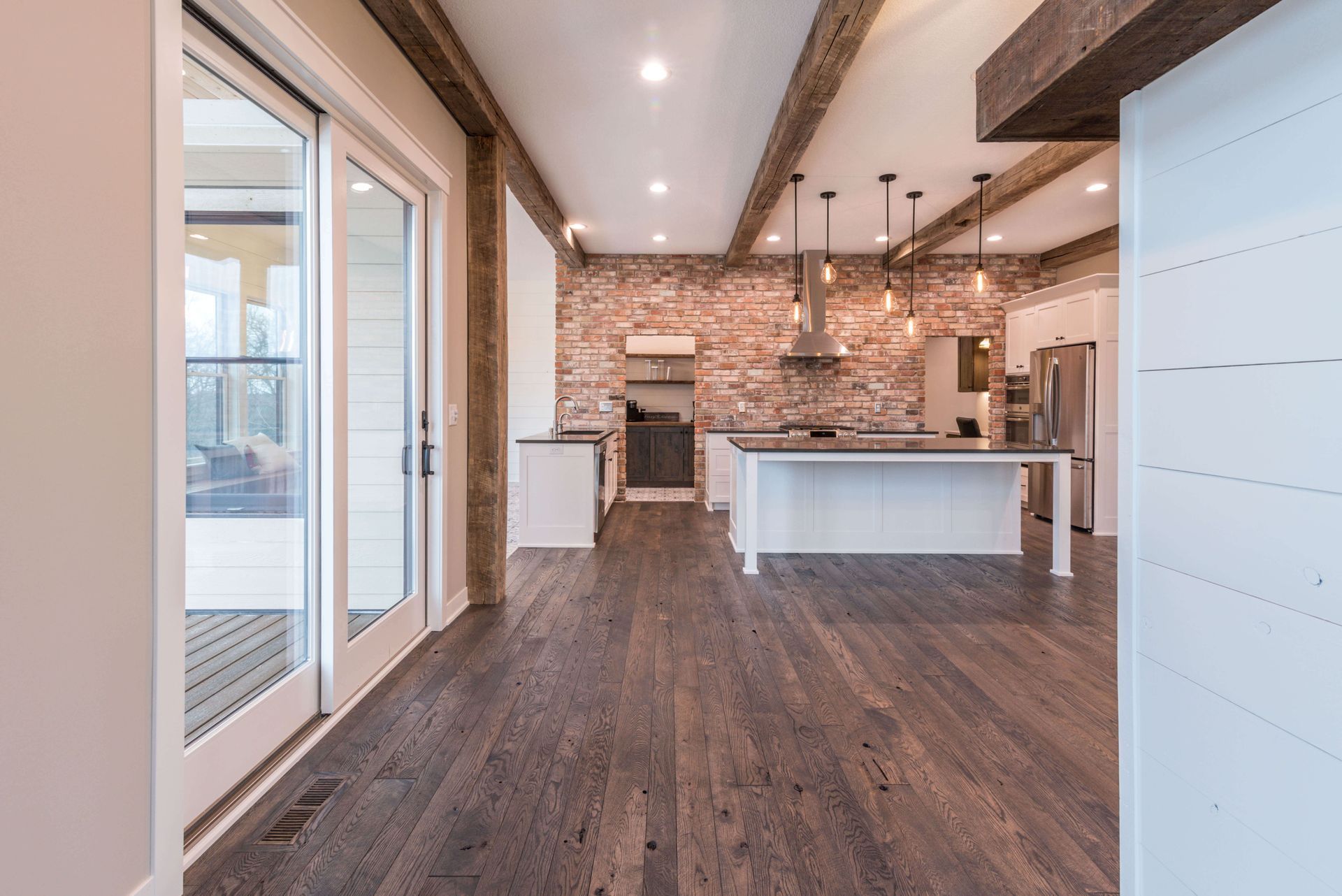 Interior view of a modern kitchen with hardwood floors, exposed brick, and wooden beams.