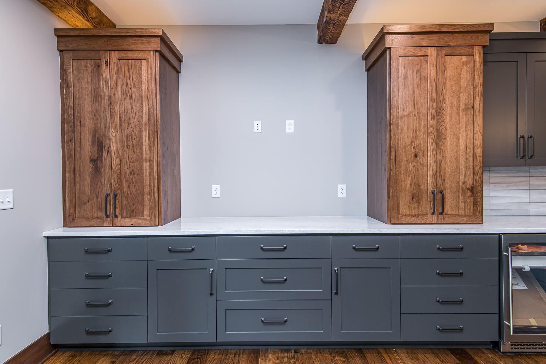 Dark wood cabinets flank a gray wall with power outlets, above gray lower cabinets.