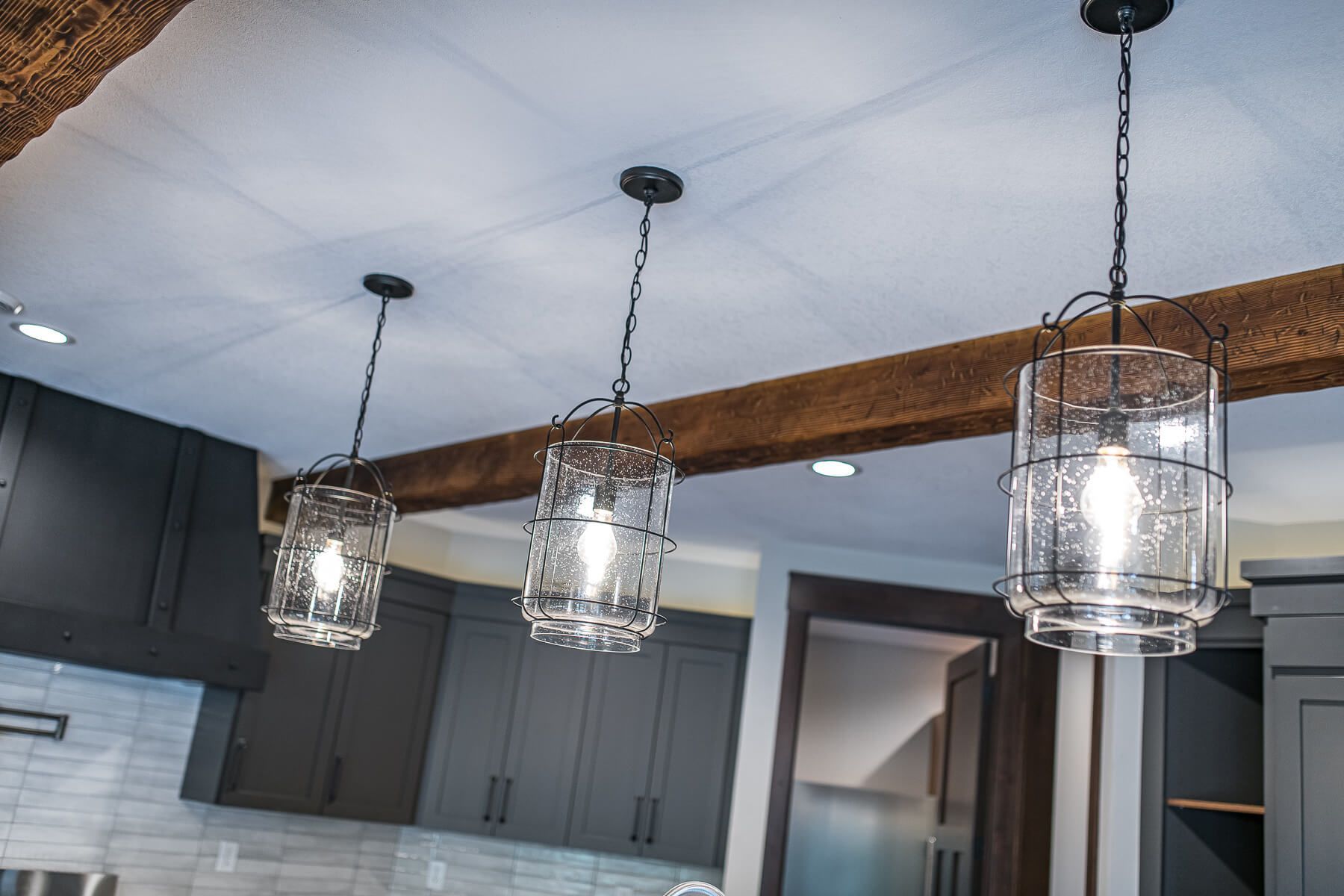 Three glass pendant lights hanging from a white ceiling, over dark gray cabinets.