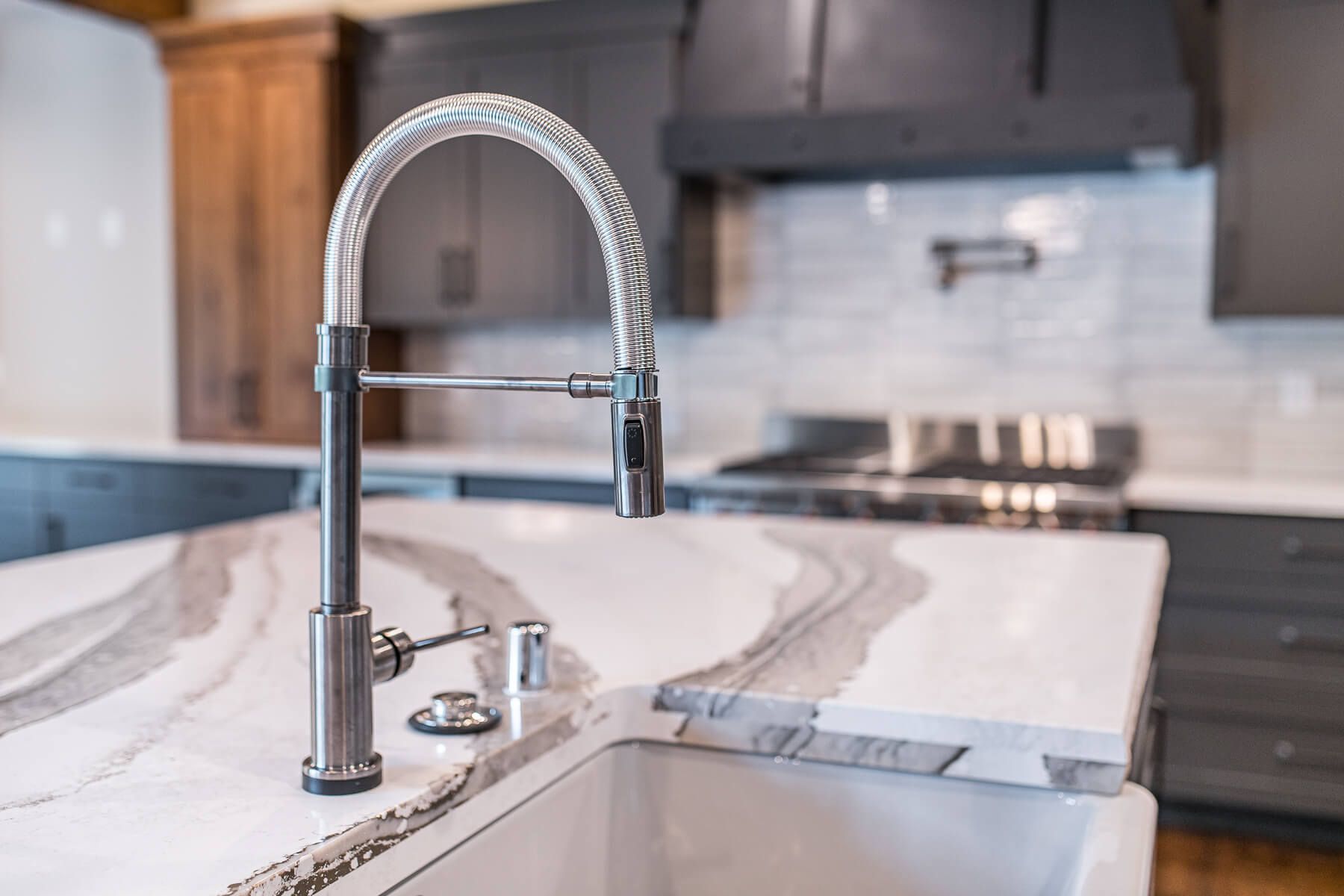 Stainless steel kitchen faucet on a white countertop with gray veining; kitchen setting with gray cabinets.