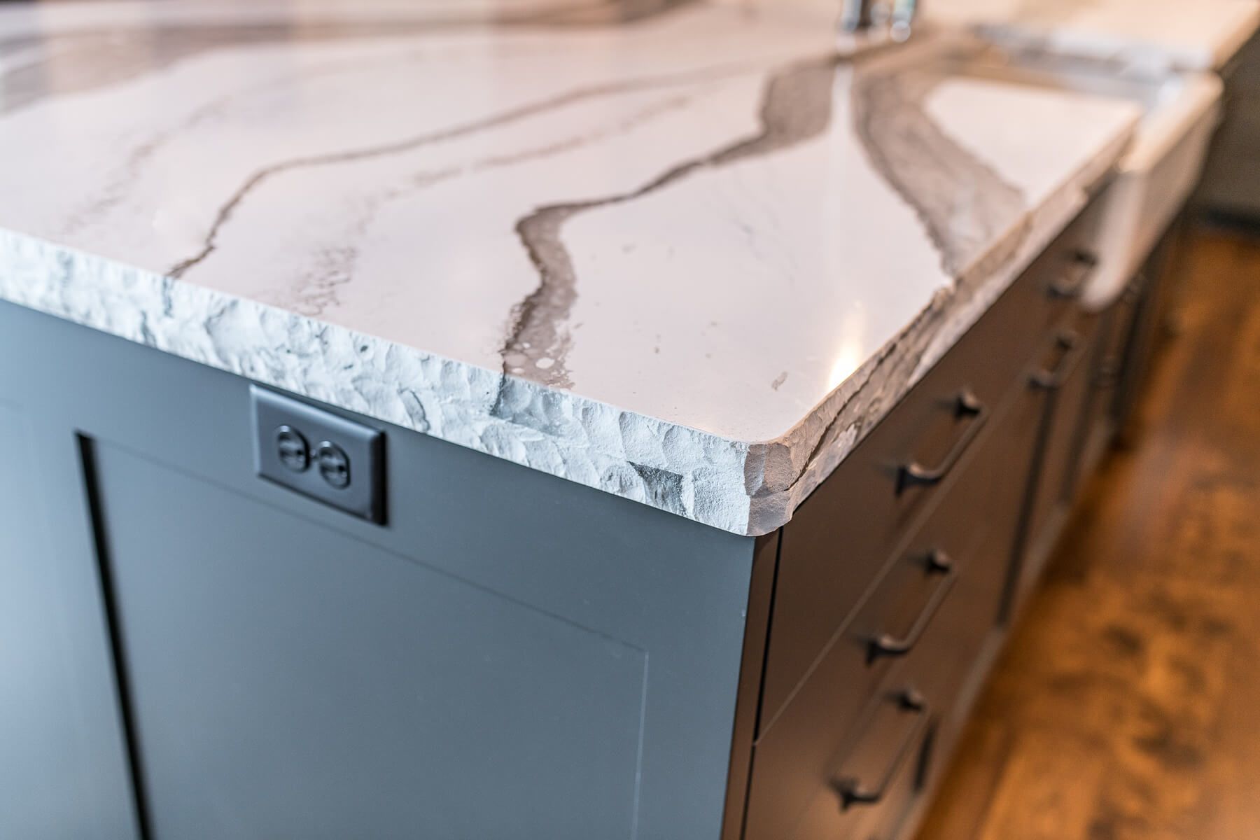Gray kitchen island with a white and gray countertop featuring a textured edge; drawers and outlets visible.