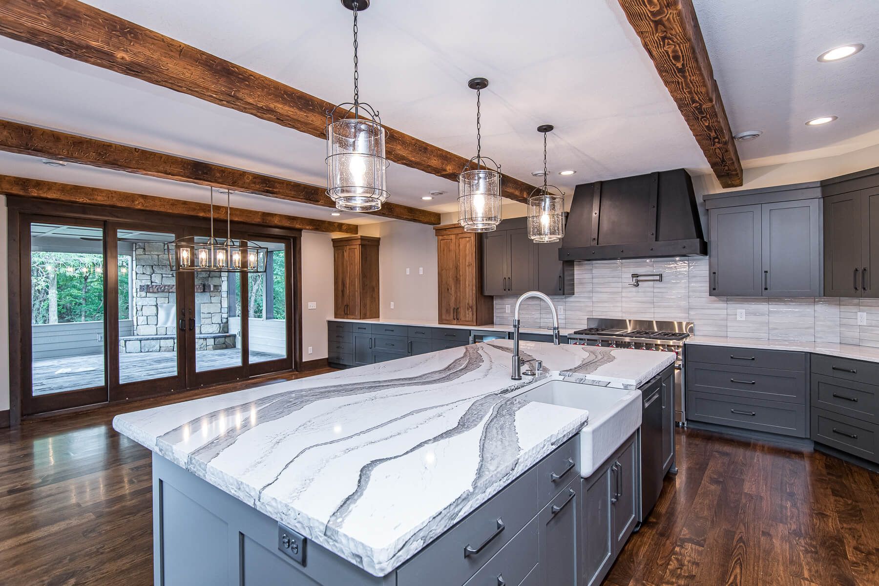 Modern kitchen with gray cabinets, marble island, wood beams, and large sliding doors.